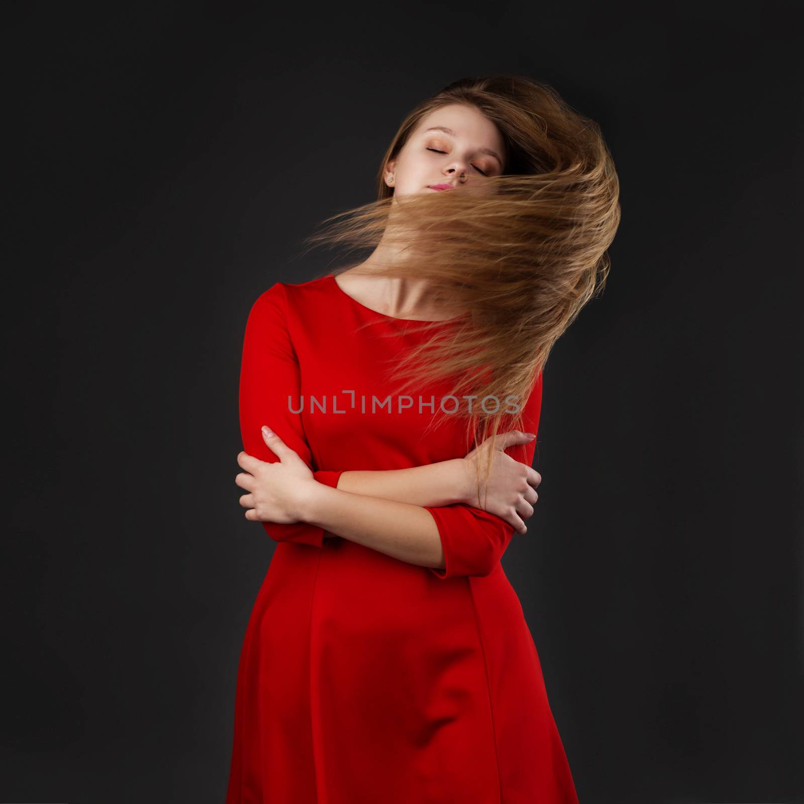 Portrait of a young beautiful girl with eyes closed in a red dress with a flying hair. Girl with long flowing hair. Hair fluttering in motion.