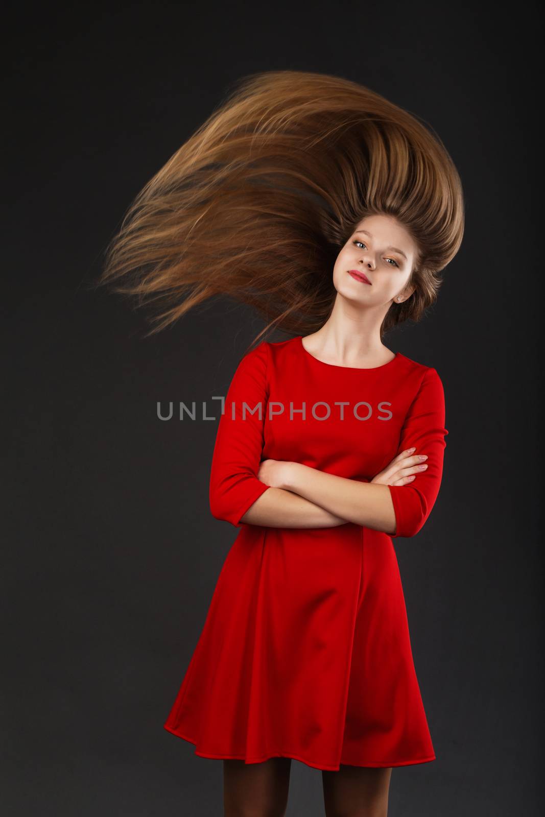 Portrait of a smiling young beautiful girl in a red dress with a flying hair. Girl with long flowing hair. Hair fluttering in motion.