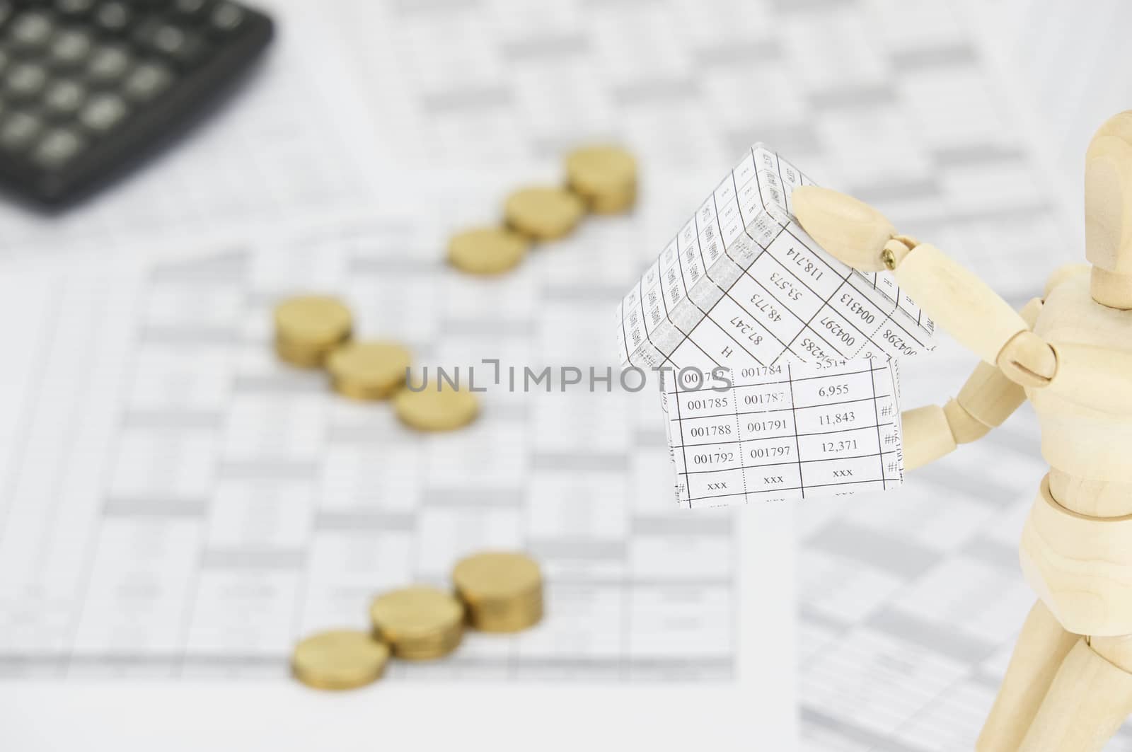 Wooden dummy holding house have blur gold coins with calculator by eaglesky