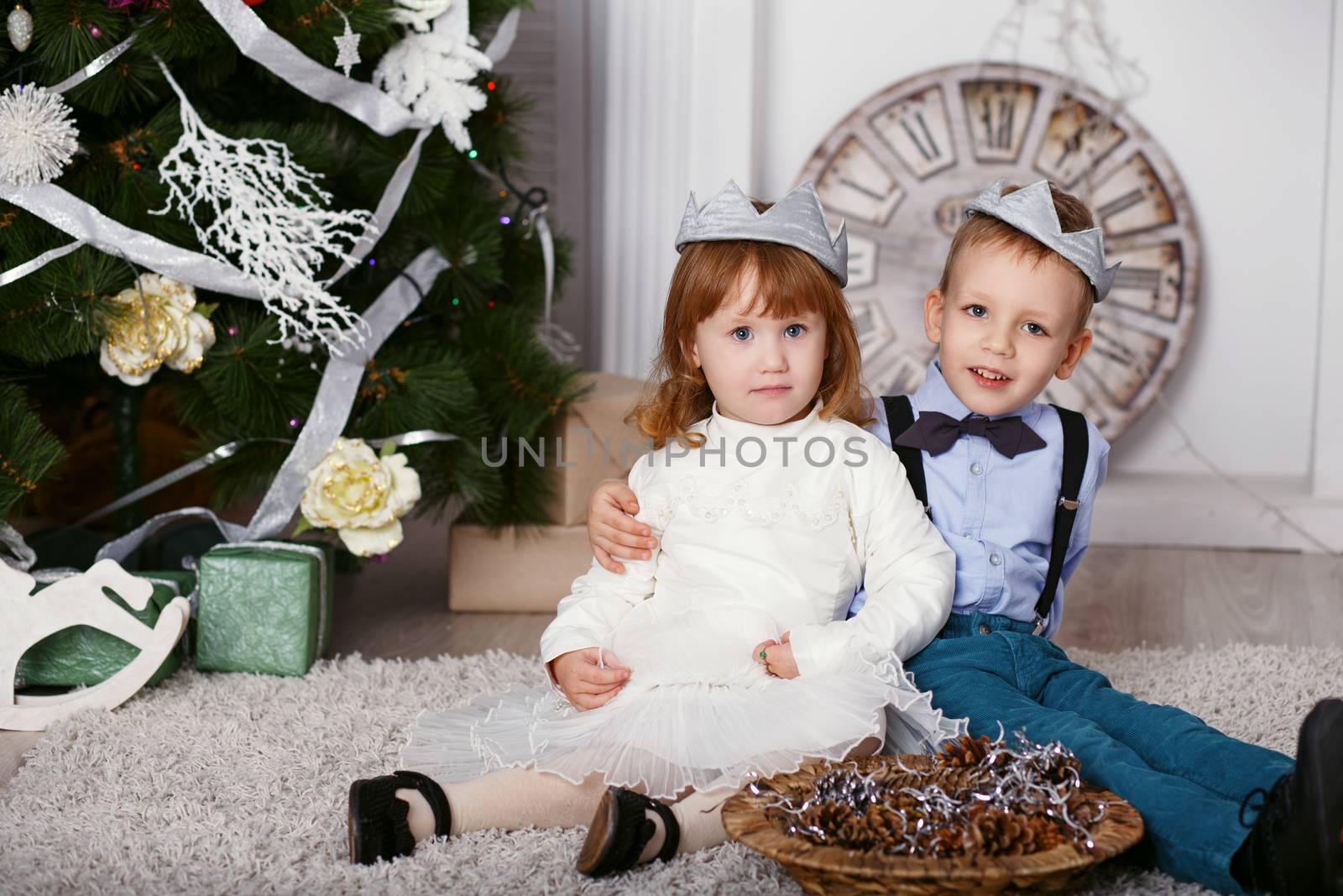 Two elegant little kids in crown. Two elegant little kids decorating Christmas tree with fir-cone. New year preparation. Happy children and family.