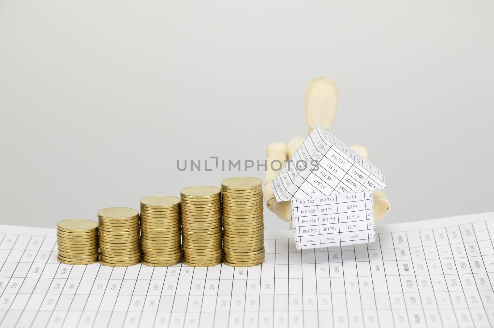Wooden dummy holding house and step pile of gold coins on finance account with white background.