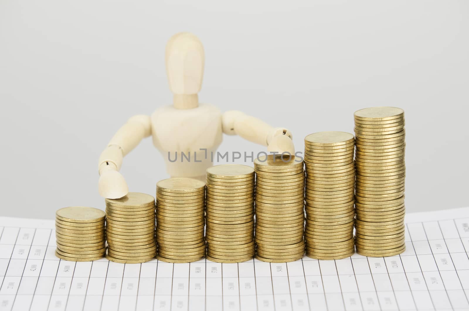 Wooden dummy touch on step pile of gold coins on finance account with white background.