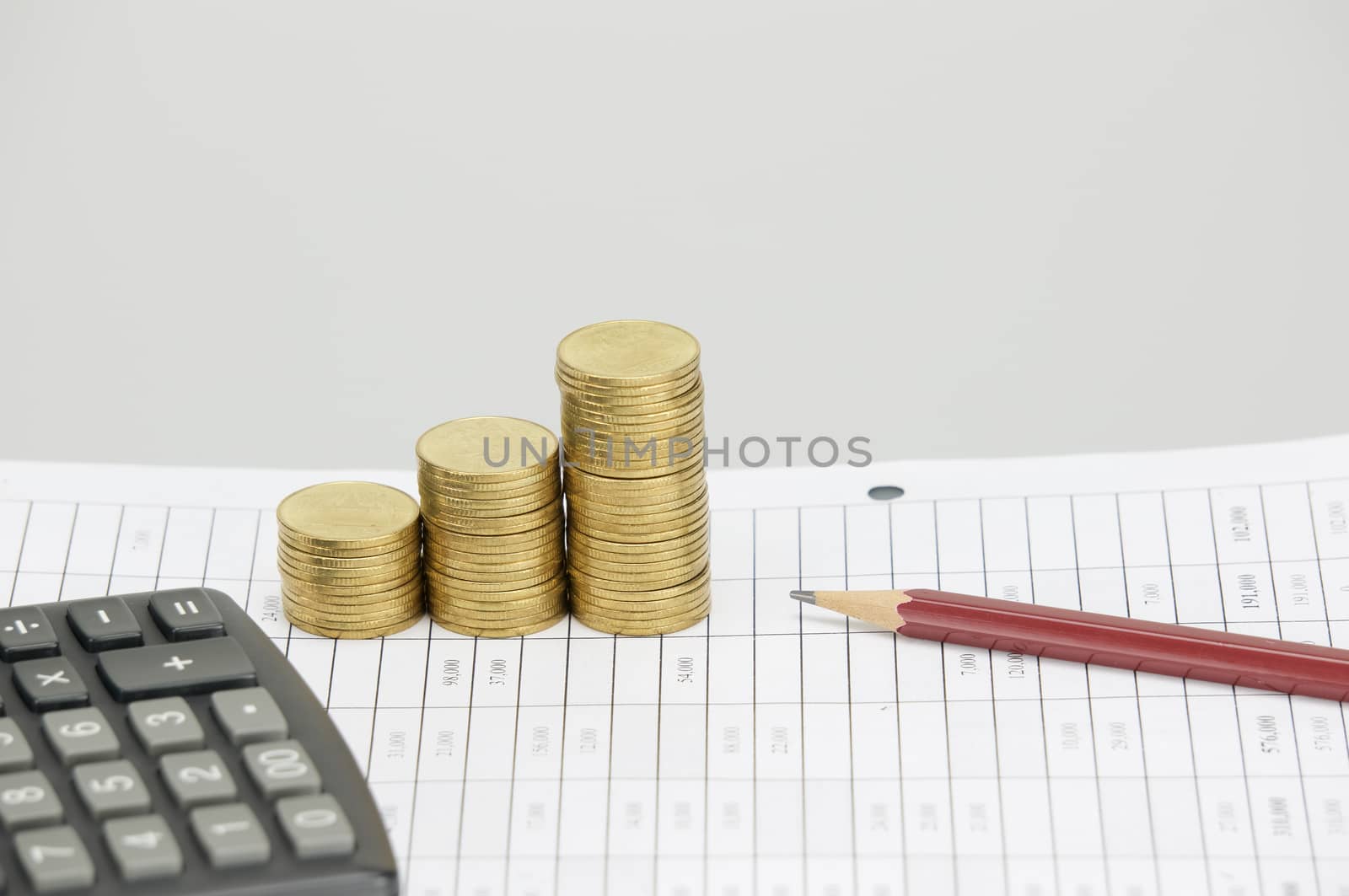 Brown pencil and step pile of gold coins on finance account and calculator with white background.