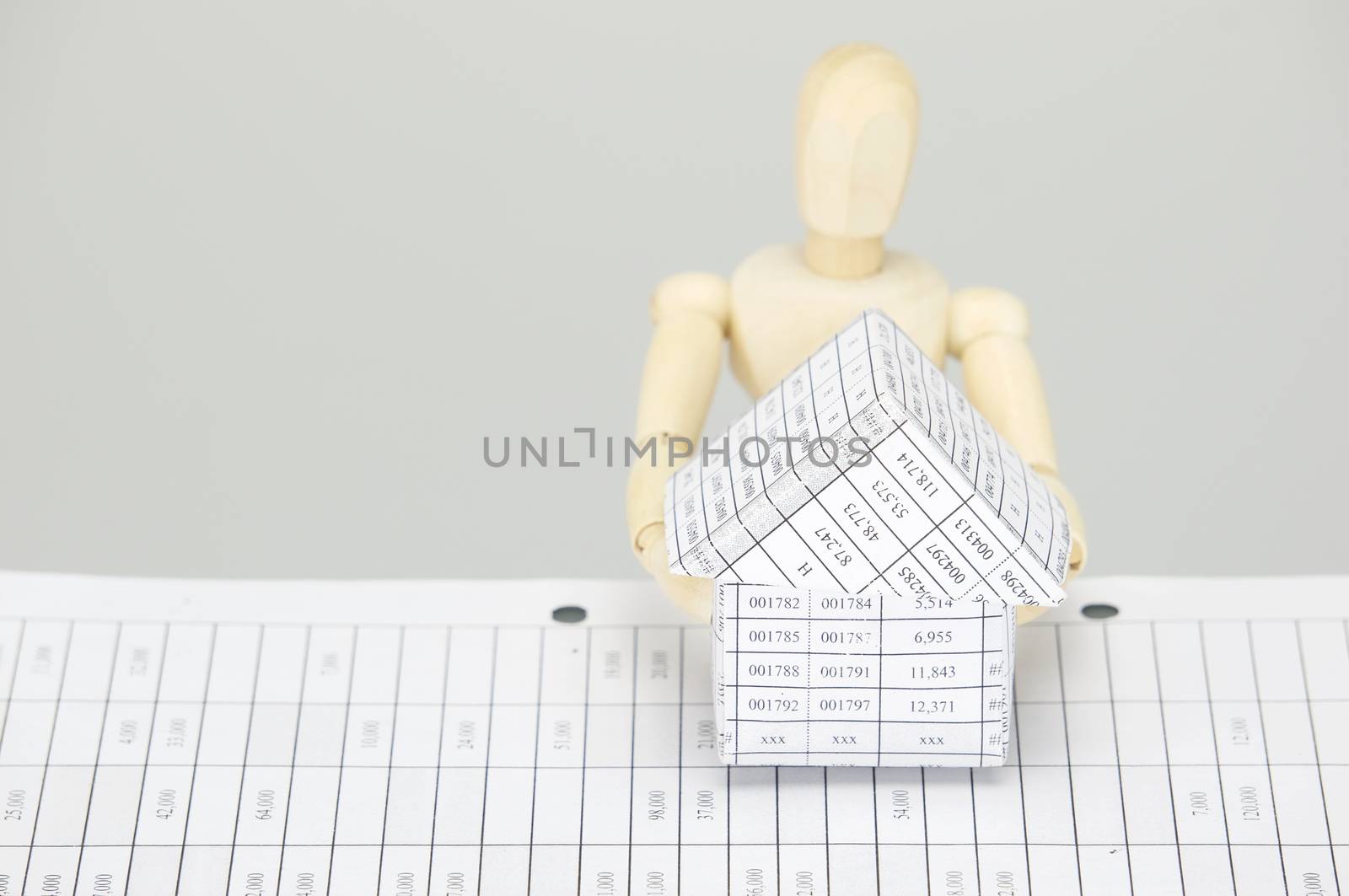 Wooden dummy holding house on finance account with white background.