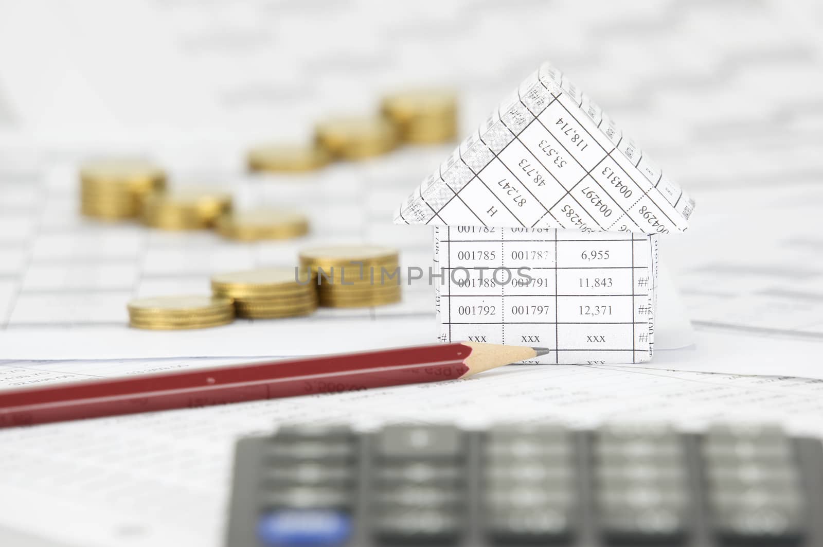 Brown pencil and house on finance account have blur calculator and step pile of gold coins as foreground and background.