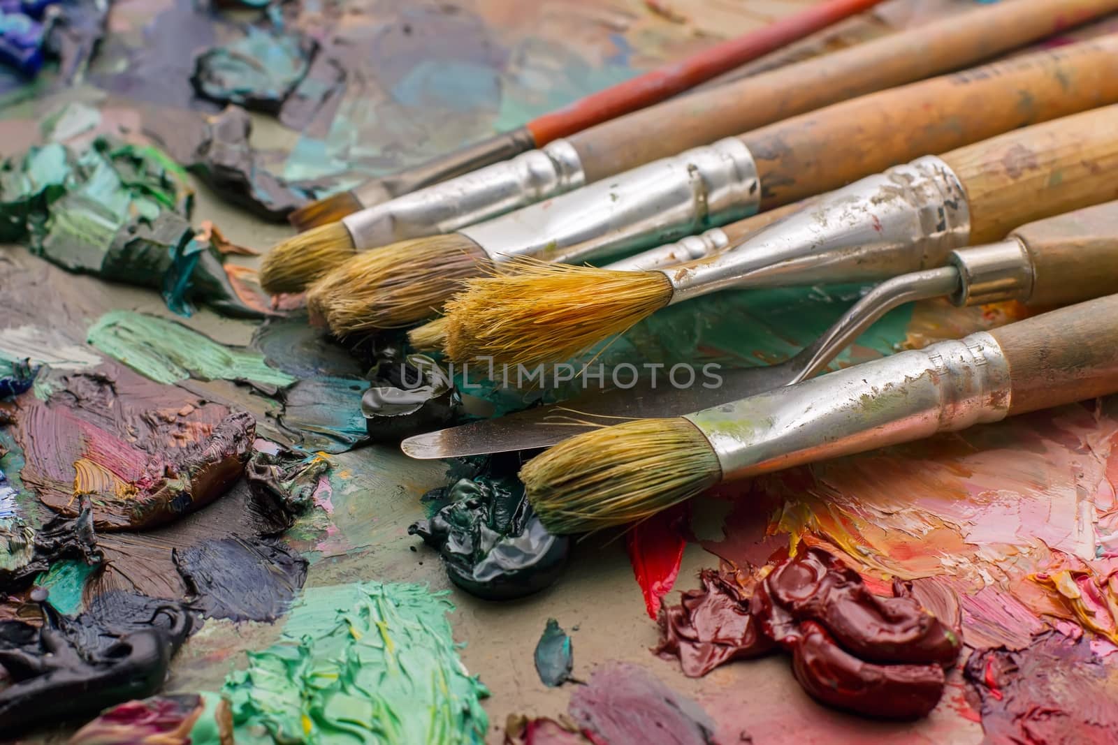 used brushes in an artist's palette of colorful oil paint for drawing and painting