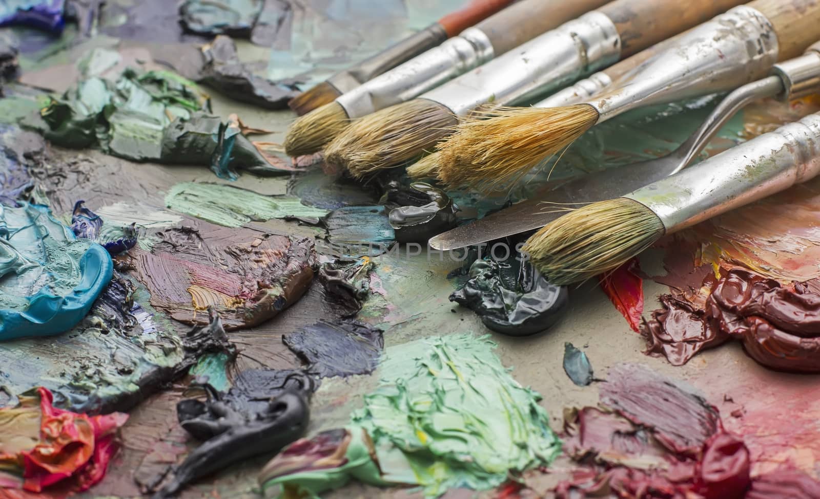 used brushes in an artist's palette of colorful oil paint for drawing and painting