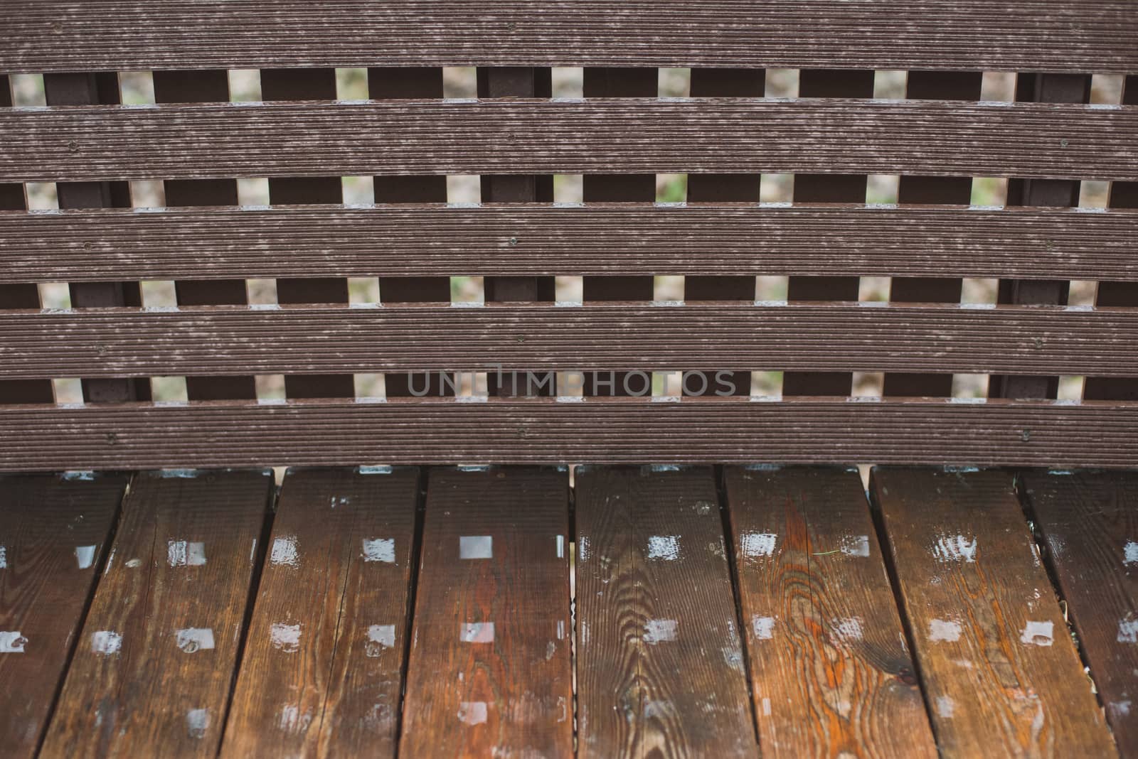 Wooden wet bench in the summer park. Closeup with reflections.