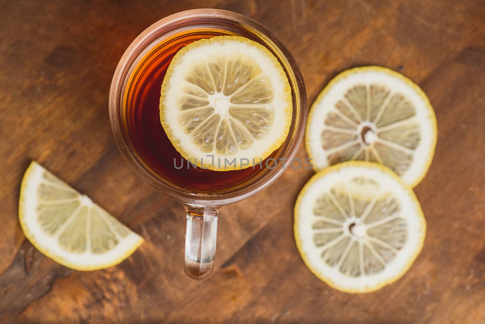 Top view of black tea with lemon in cup and on wooden plank table.