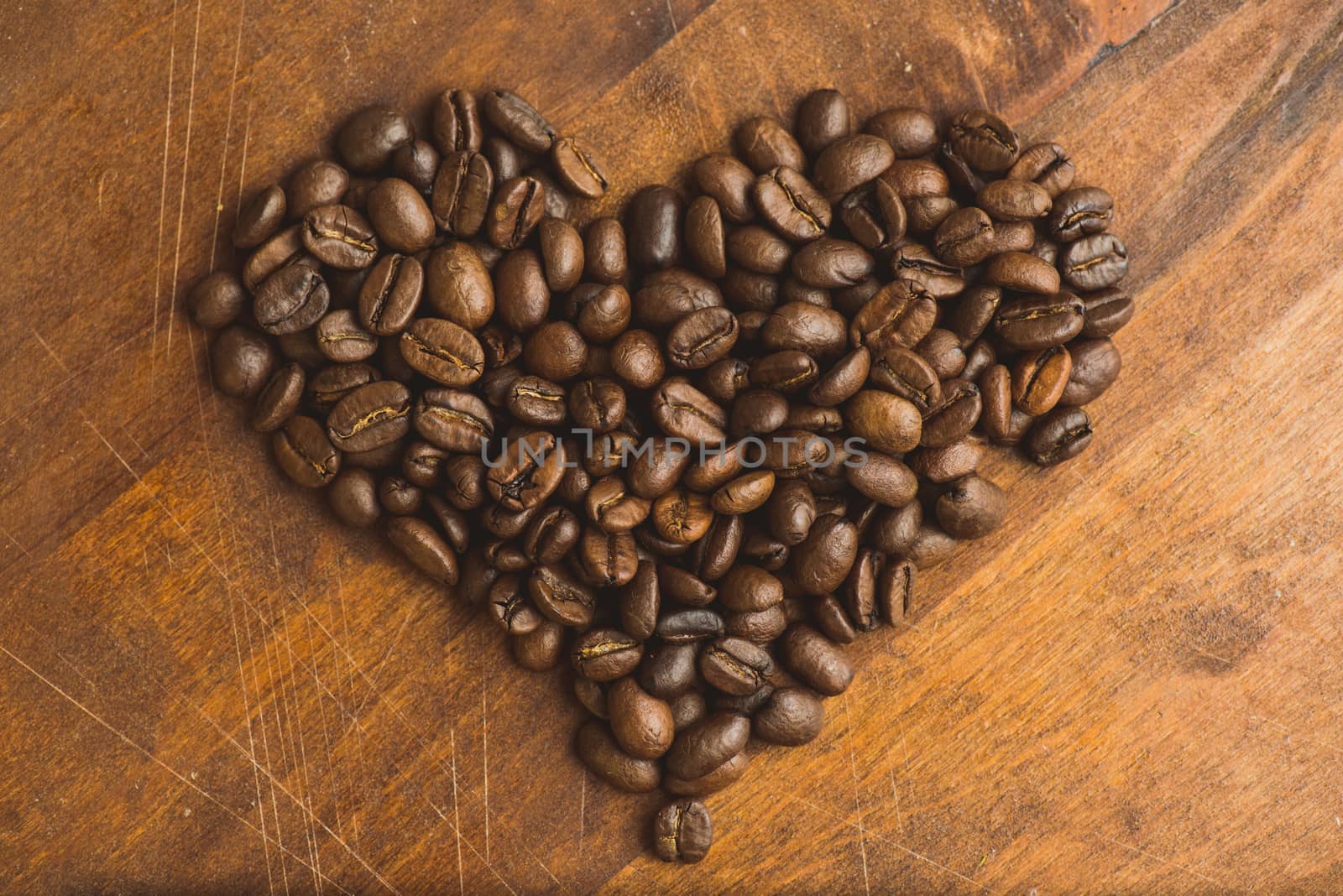 Brown coffee beans in  shape of heart, closeup of macro coffee beans for background and texture. On brown wooden board. by skrotov