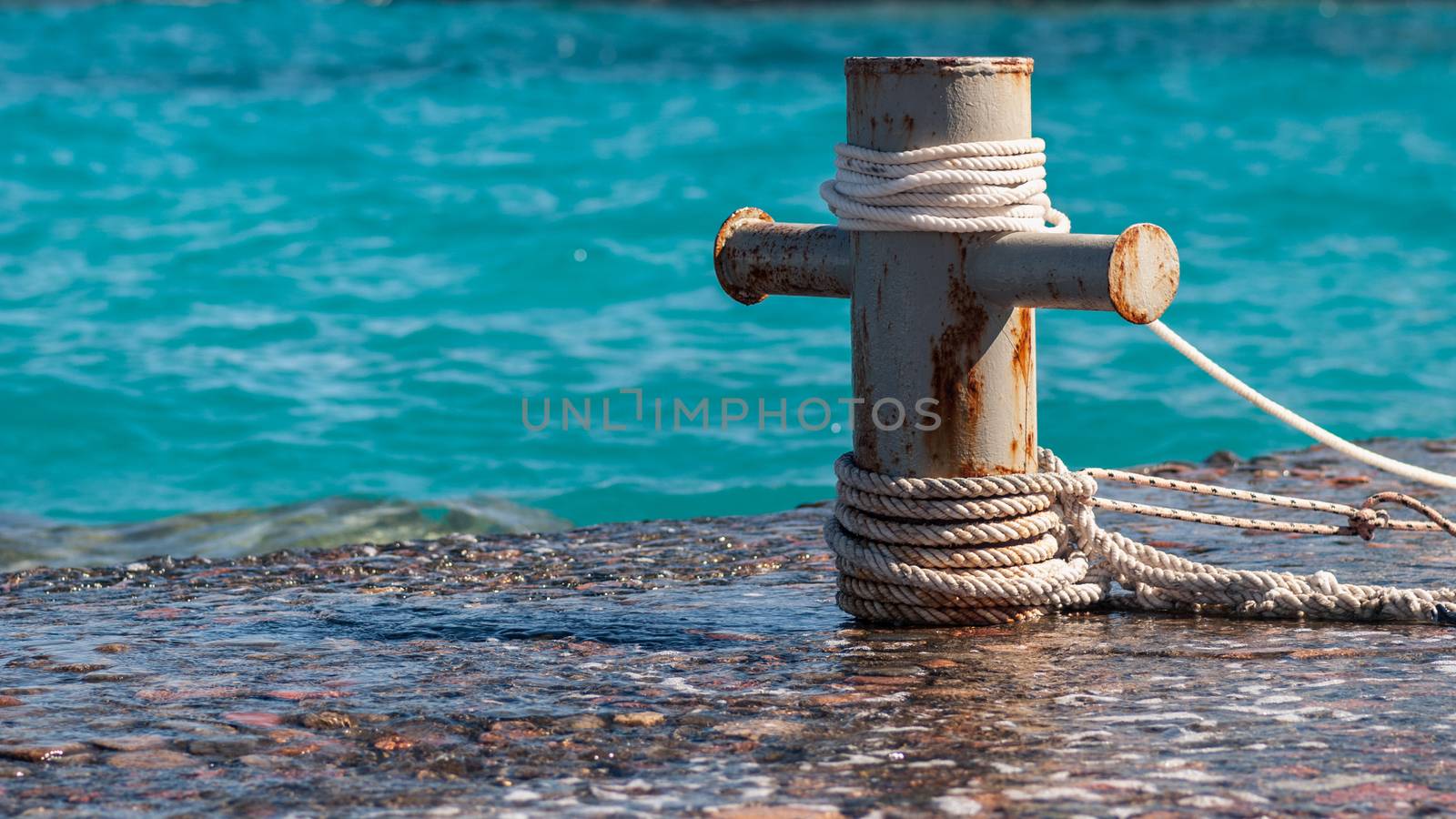 Rusty mooring bollard with ship ropes and  clear turquouse sea ocen water on background by skrotov