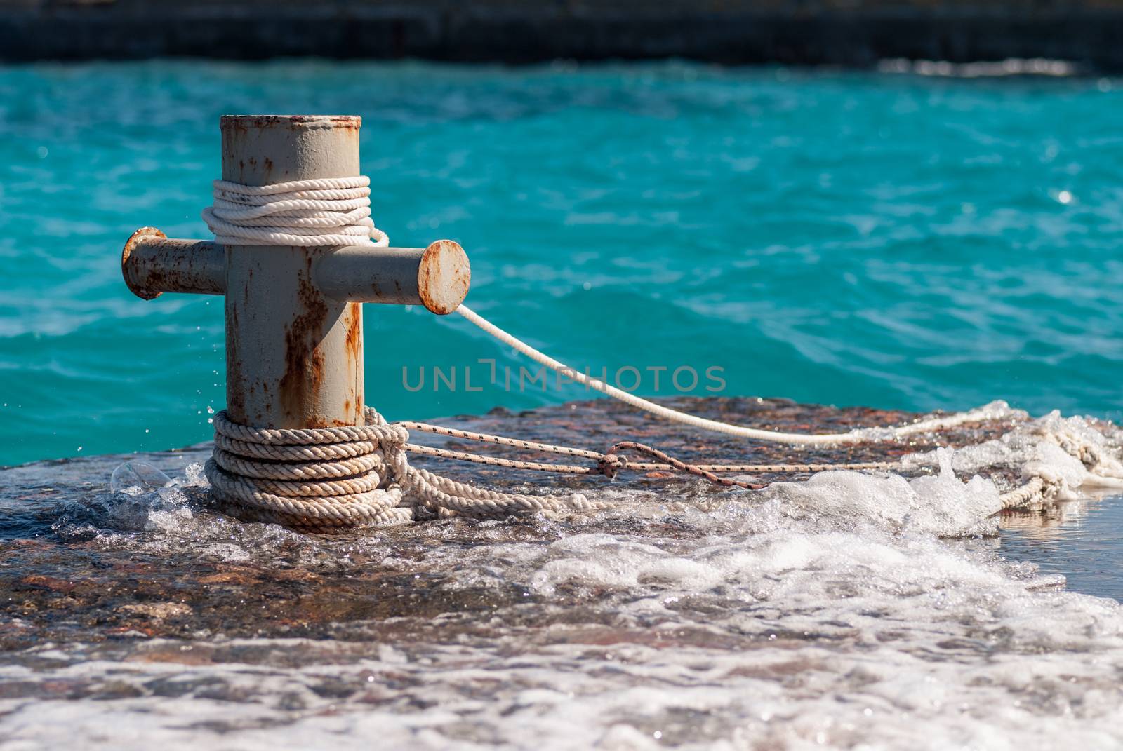 Rusty mooring bollard with ship ropes and  clear turquouse sea ocen water on background by skrotov