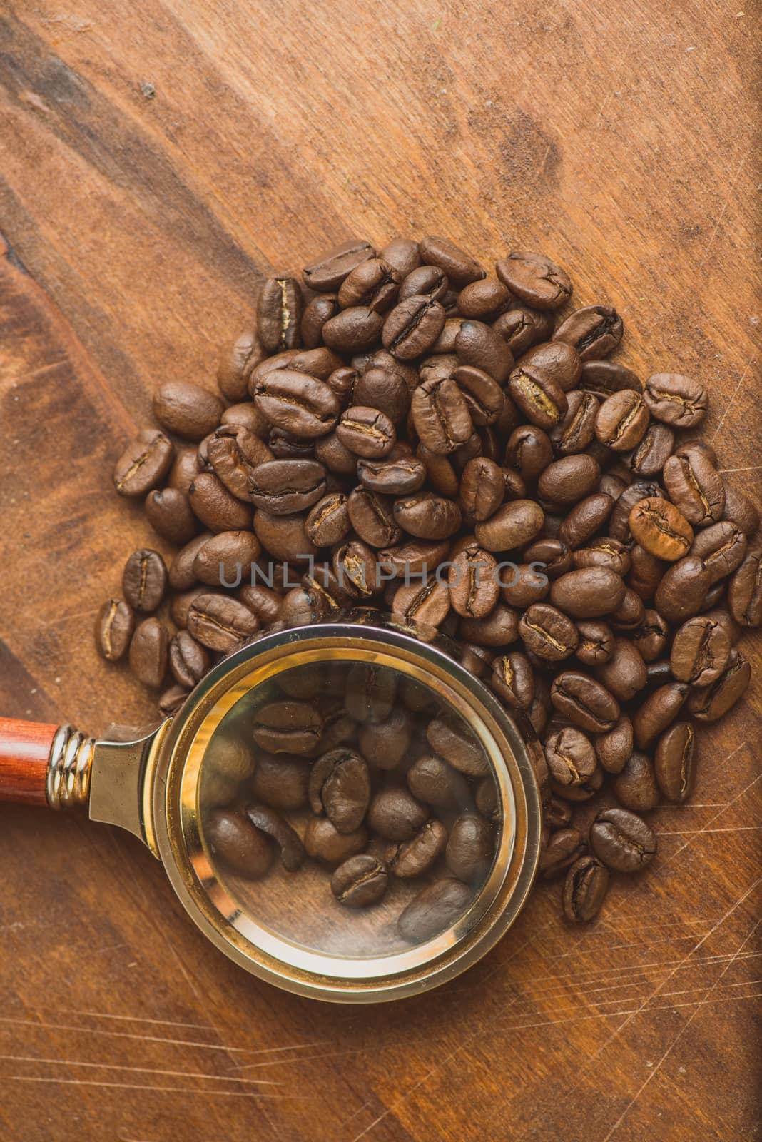 Brown coffee beans in circle shape, closeup of macro coffee beans for background and texture. On brown wooden board with magnify glass. Copyspace.