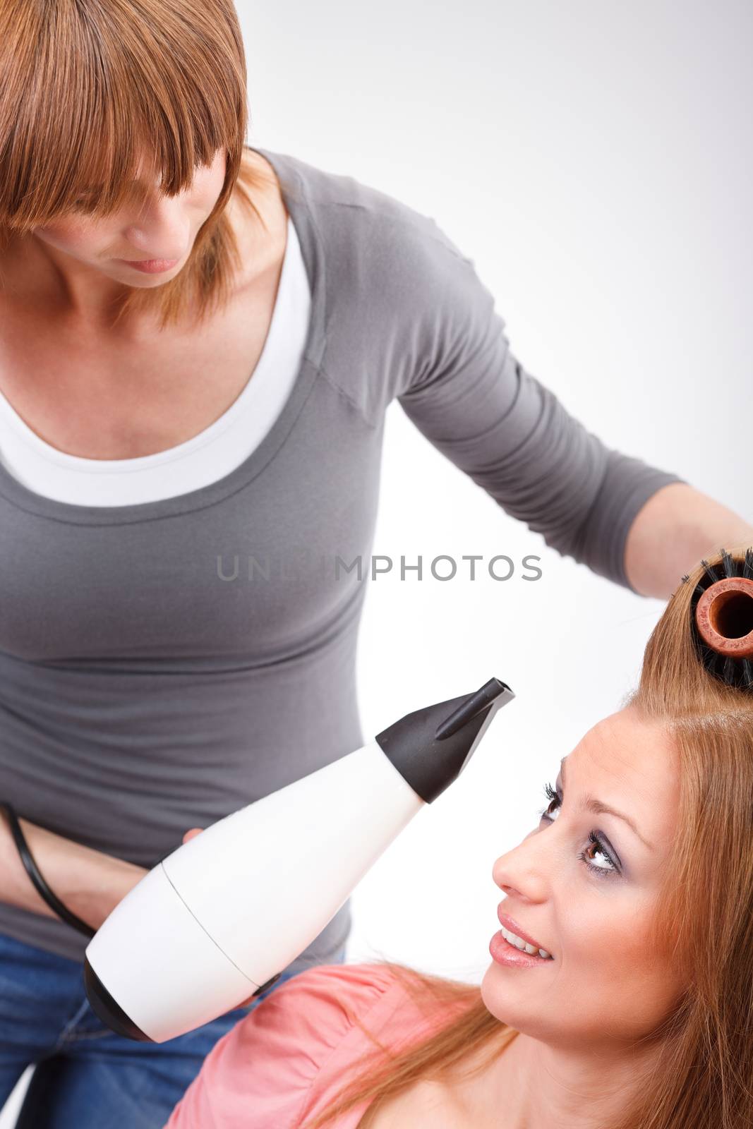 Beautiful young hairdresser drying woman hair