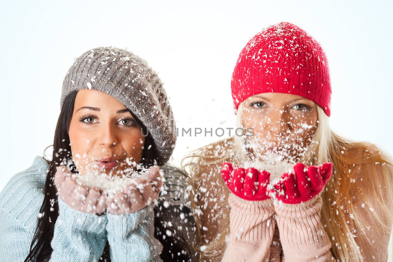 Beautiful girls in warm clothing holding and blowing snow