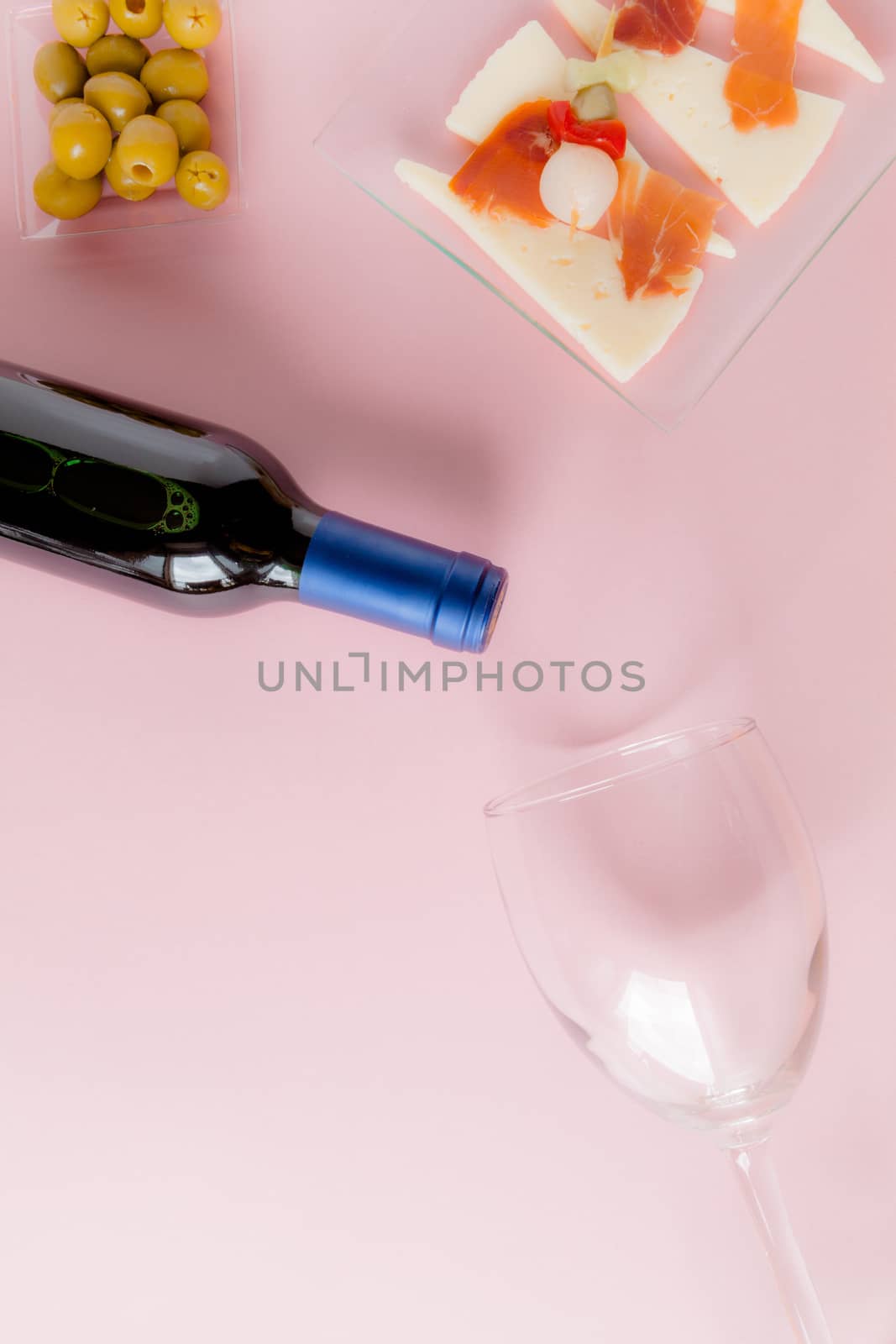 Top view of a bottle of red wine, a glass, olives, cheese and ham