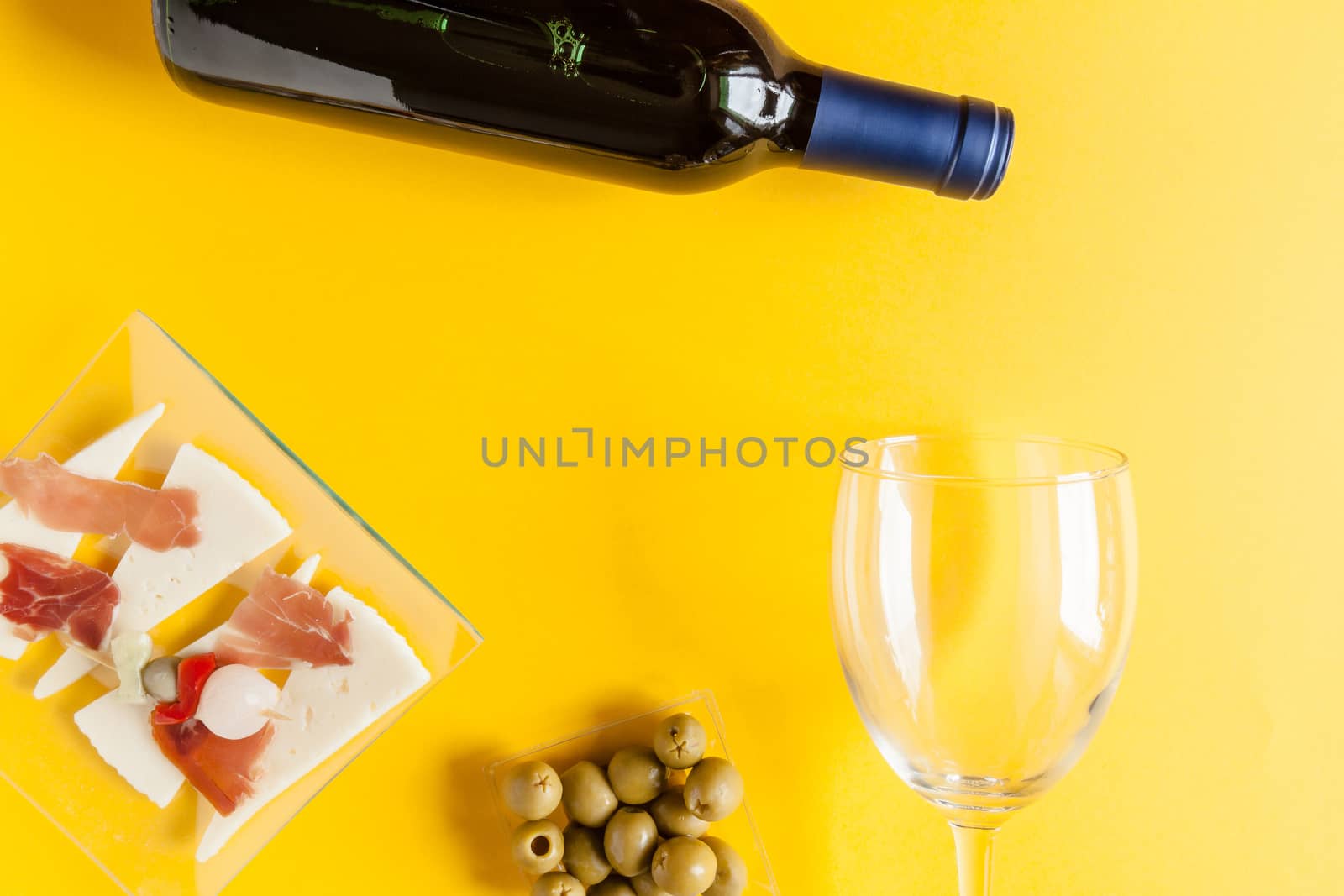 Top view of a bottle of red wine, a glass, olives, cheese and ham