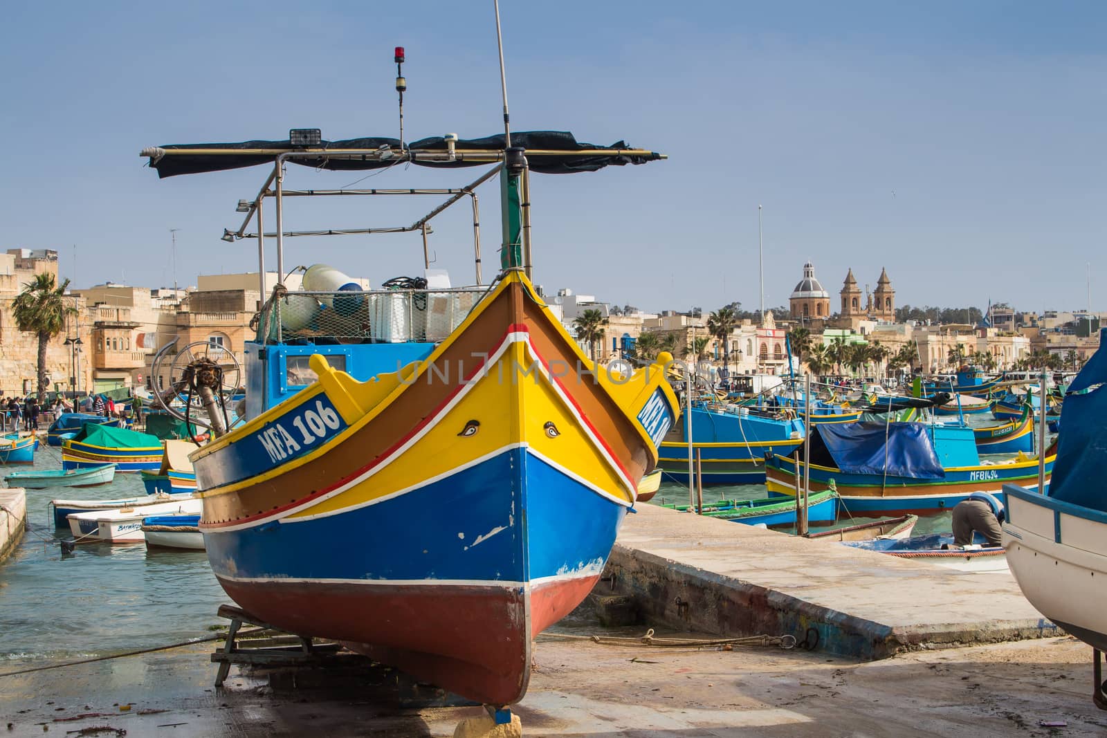 Port Marsaxlokk, fishing village at the island Malta. Multicolored traditional fishing boat with painted eyes. Houses and church in the background.