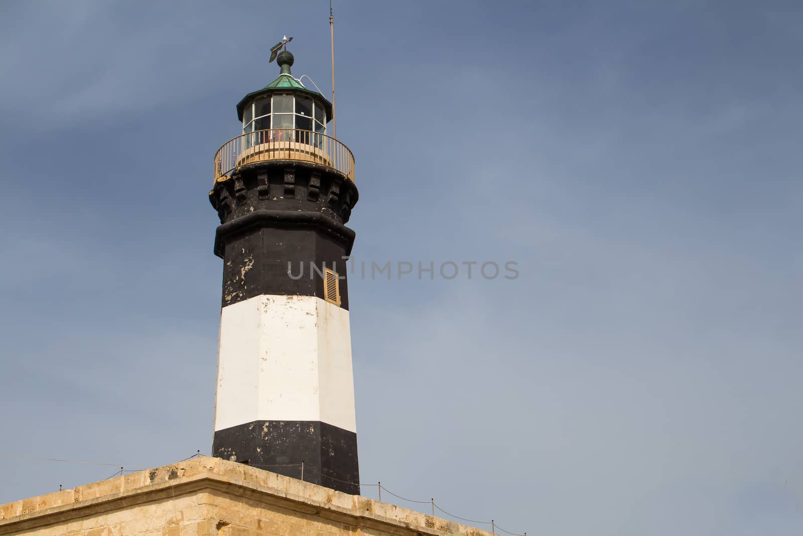 Black and white tower of the lighthouse at the island Malta, Delimara point in the south-east part of the island. Cloudy sky in the background.