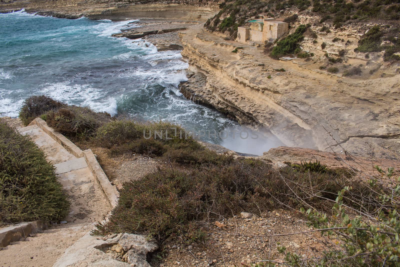 Rocks on the coast of Mediterranean sea, south-east of island Malta. Blue water of the sea, white waves, breaking at the rocks of the island.