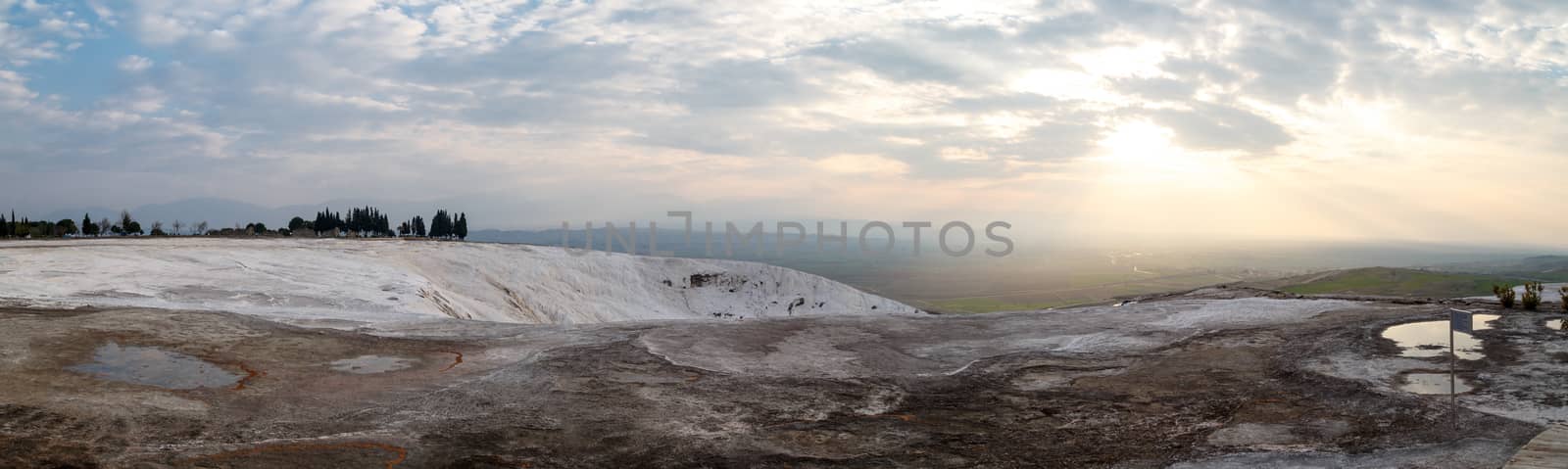 Panoramic view of Pamukkale Travertines with geographical formations on cloudy sky background at sunset time.