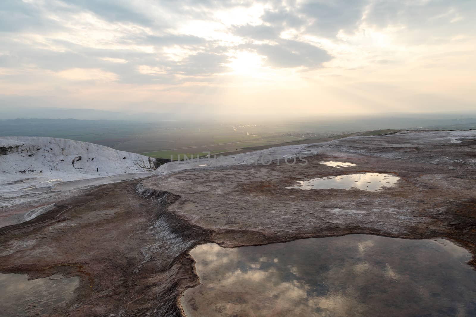 General view of Pamukkale Travertines with geographical formations on cloudy sky background at sunset time.