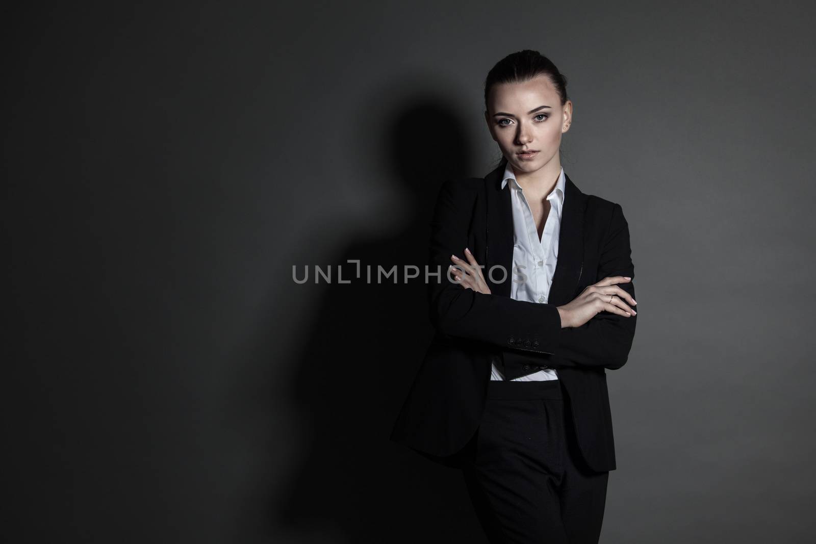 Portrait of young businesswoman in black suit on dark background