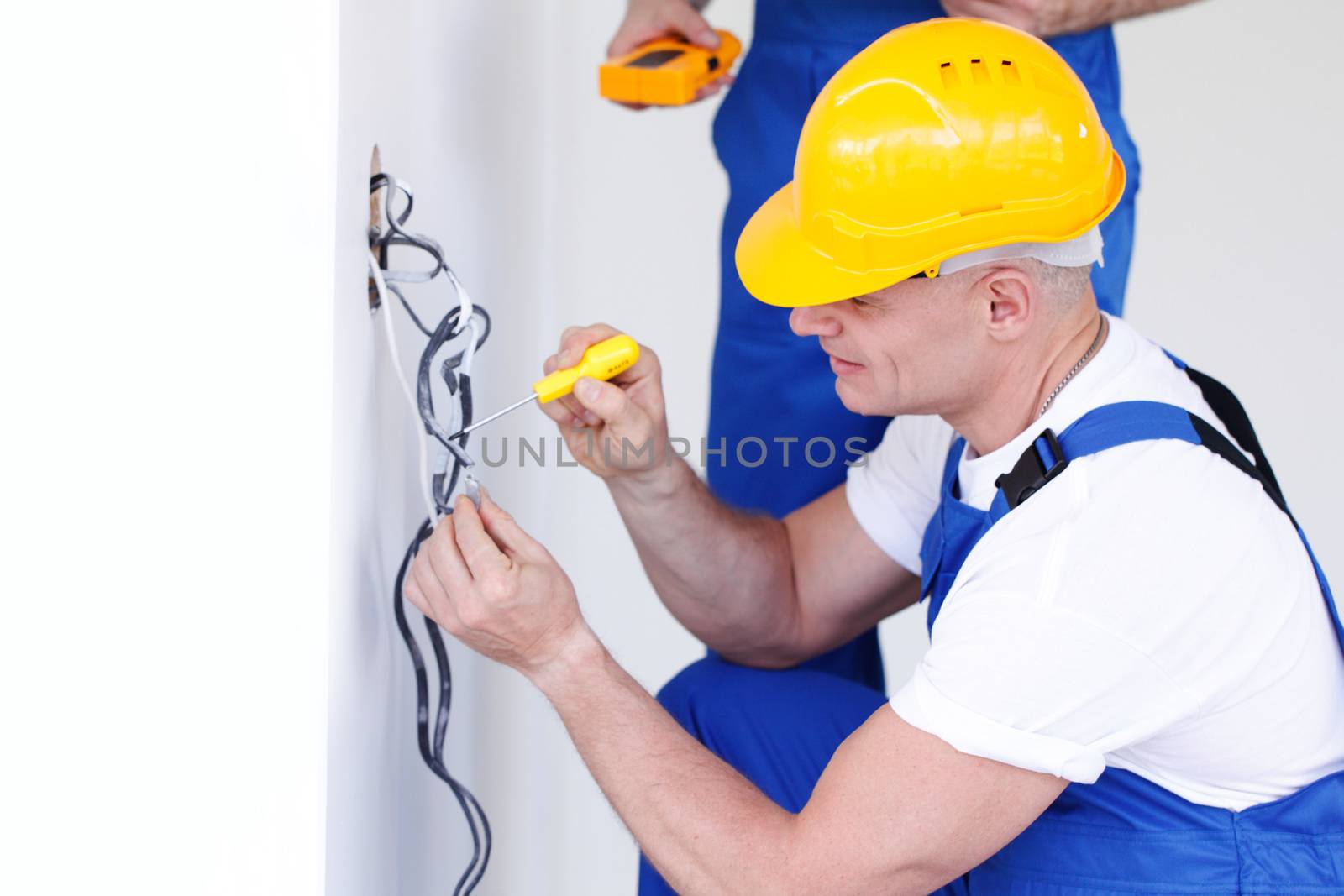 Two builders in helmets working with electricity indoors