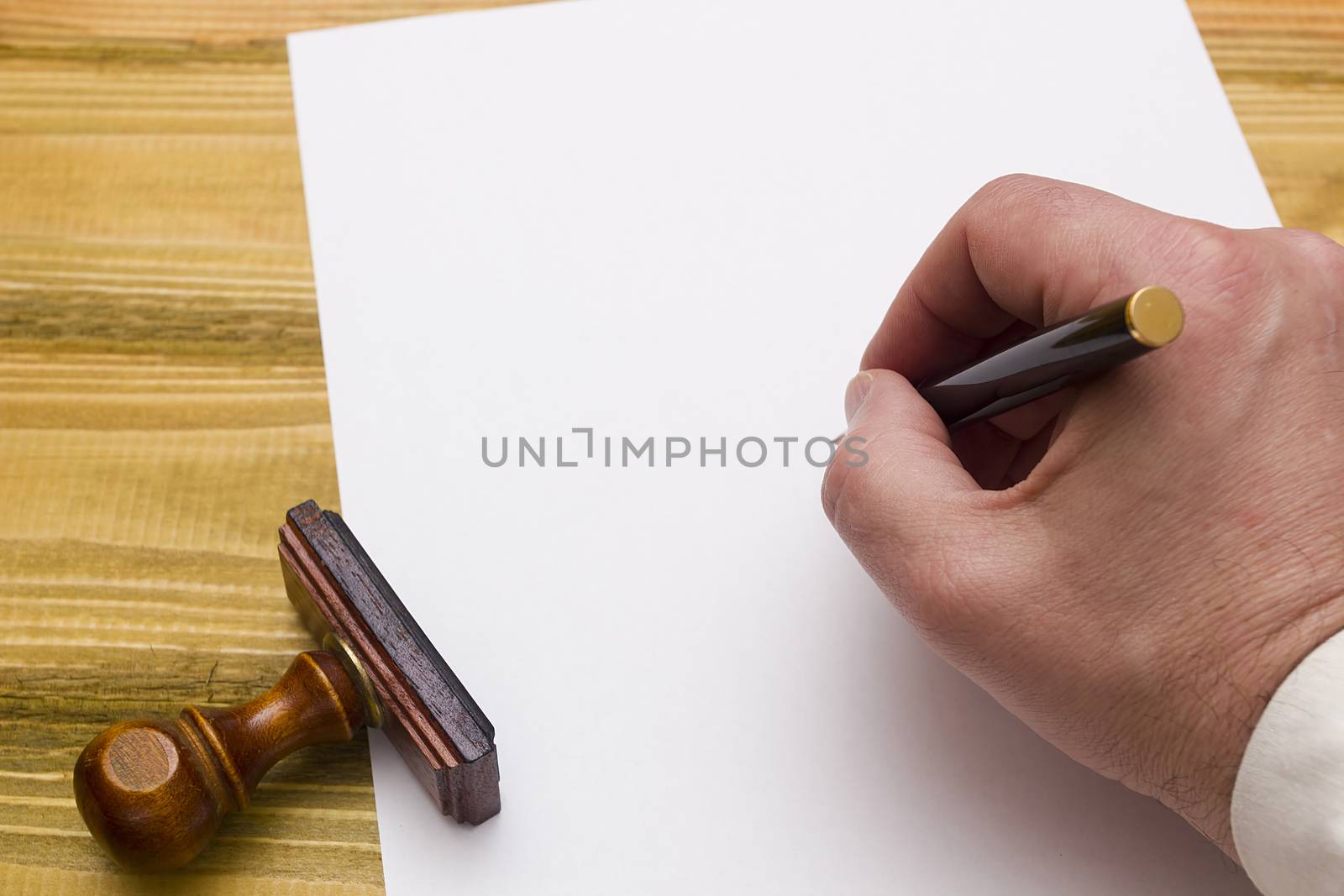 Hand with pen writing on a blank paper on a wooden table