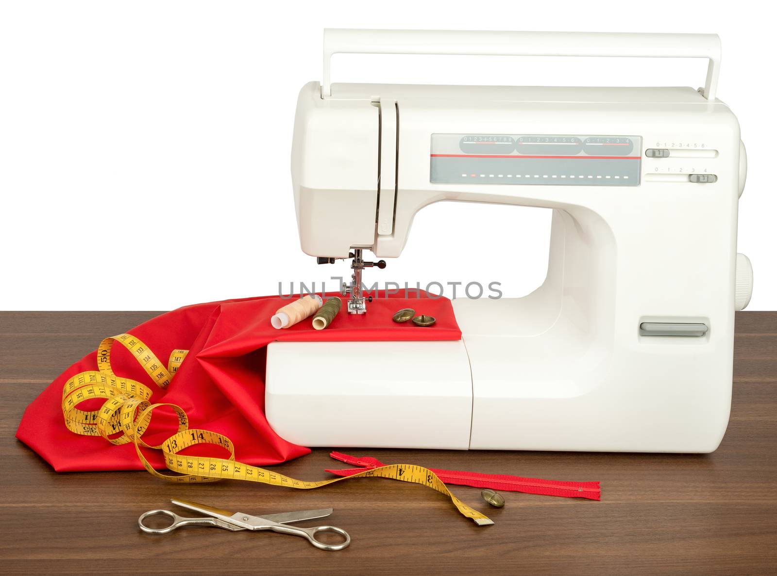 Sewing machine with red fabric, threads and scissors isolated on wood table. Front view
