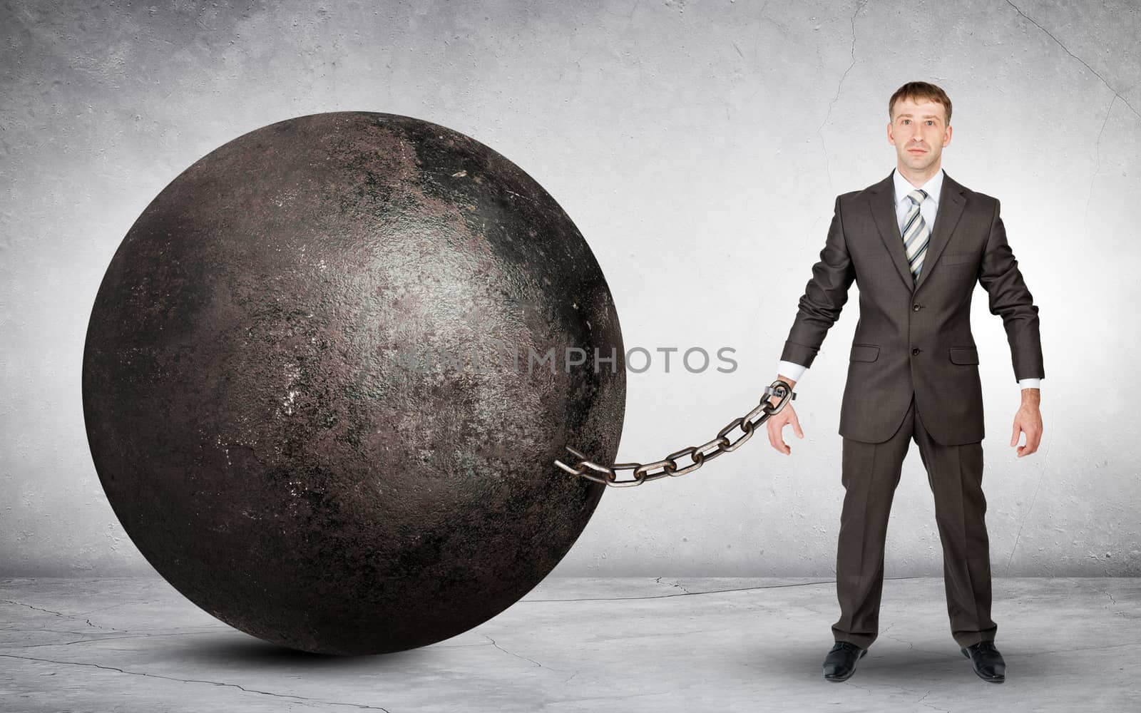 Businessman chained to large ball on grey background