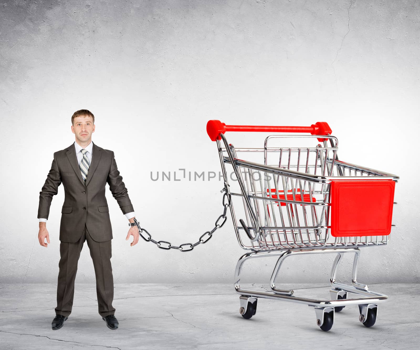 Businessman chained to shopping cart on grey background