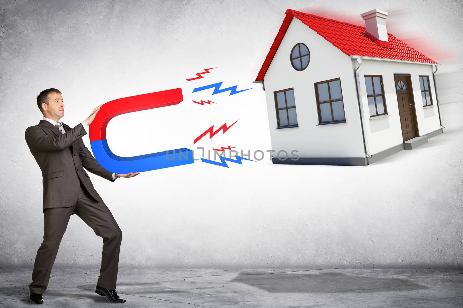 Businessman in suit holding big magnet attracting house