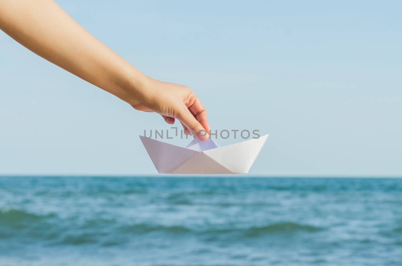 Female hand holding paper boat on the sea background by koson