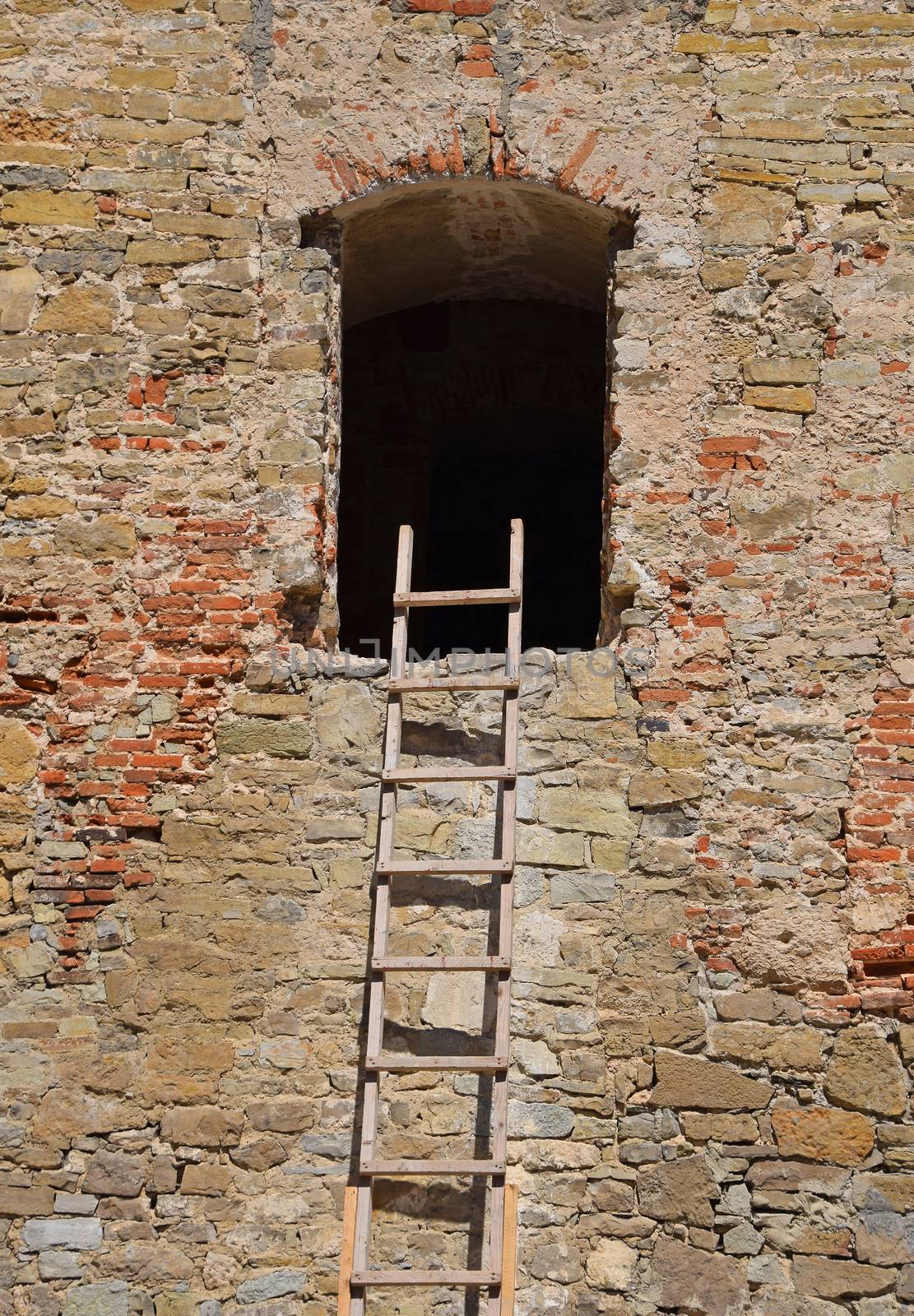 Wooden ladder next to empty window of old vintage stone wall of medieval building