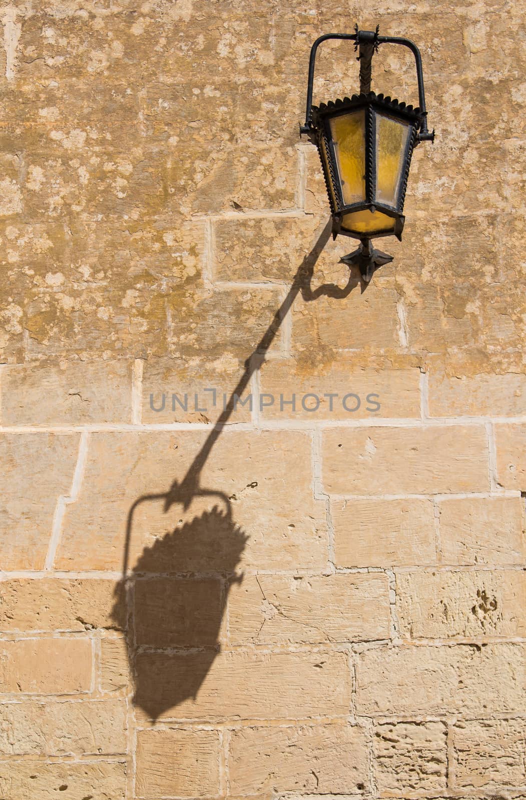 Old black lantern with yellow glass and its shadow on the stone wall. Former capital of island Malta - Mdina.