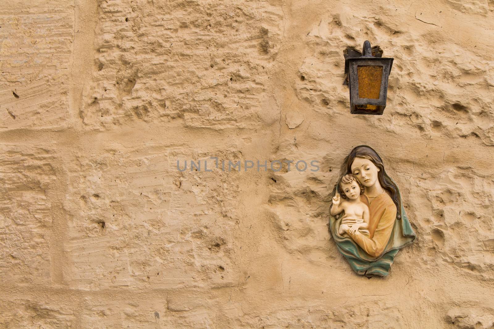 Small statue of Virgin Mary and a Child under a lantern on a texture wall of a house at the mediterranean island Malta.