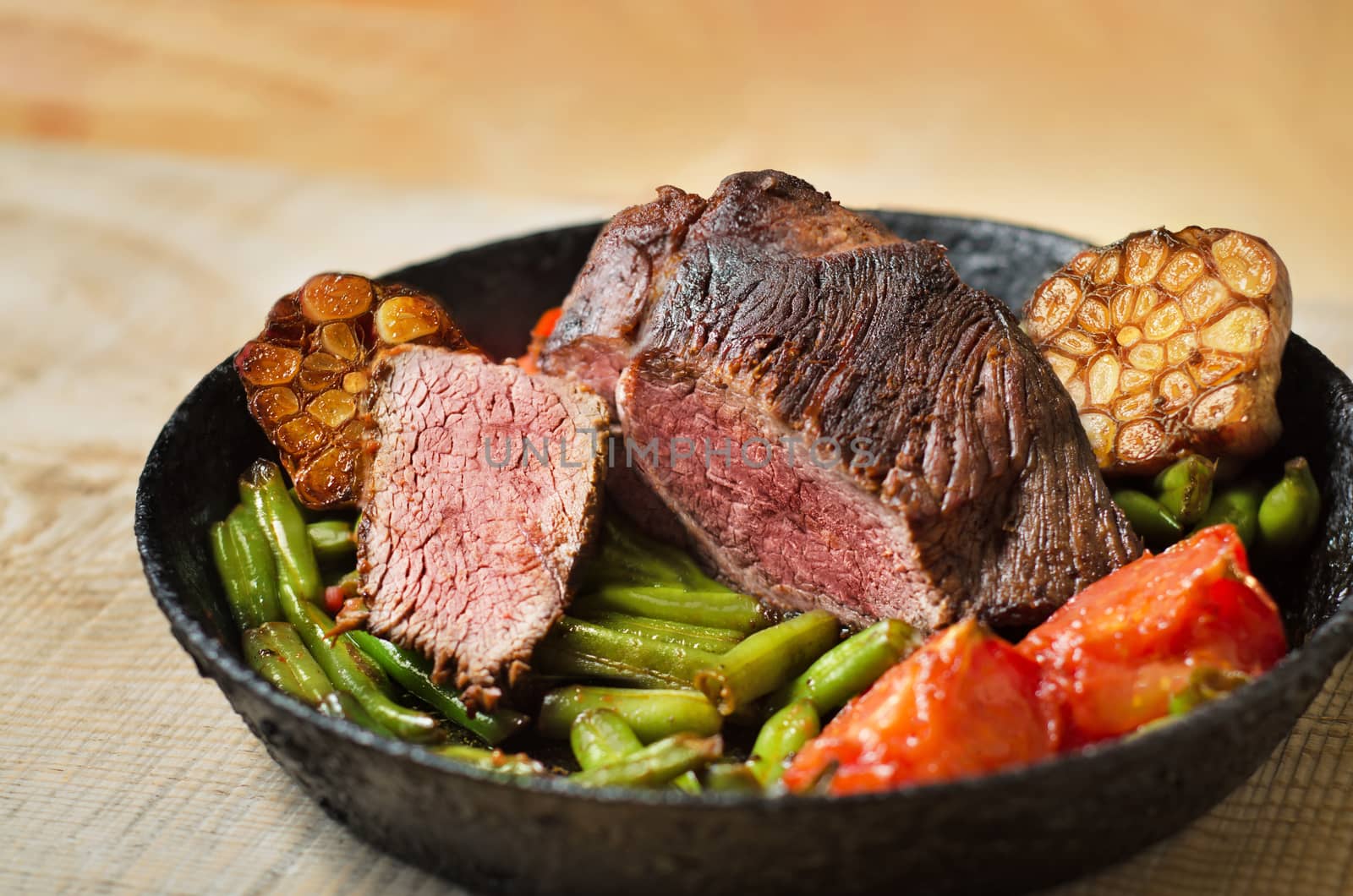 Roast beef with vegetables in a cast iron skillet and boards. Cut the meat, garlic,green beans,tomatoes and bokeh.