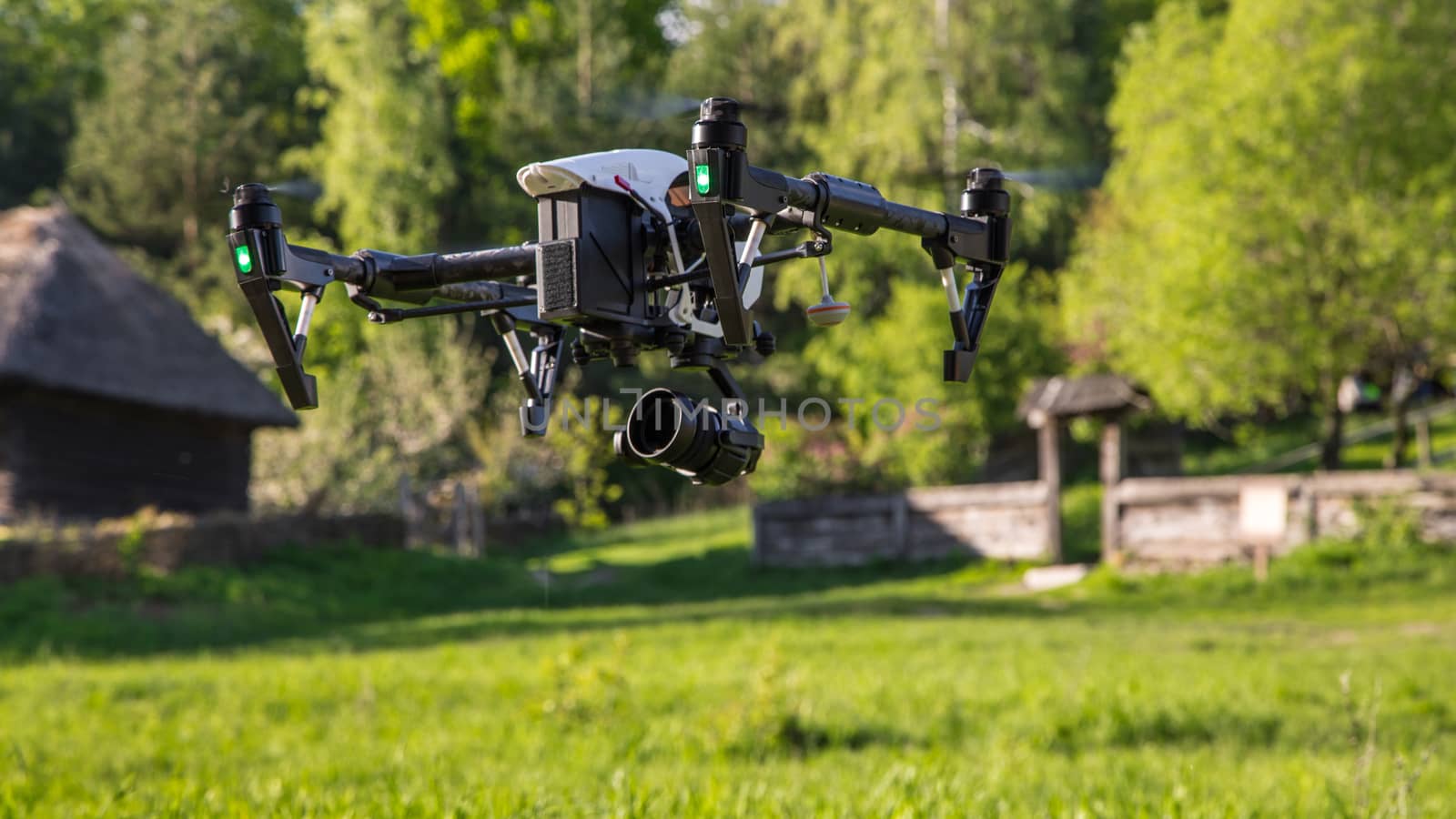 Flying copter with raised chassis and a camera is filming in the countryside. Photographed close-up with the bottom point.