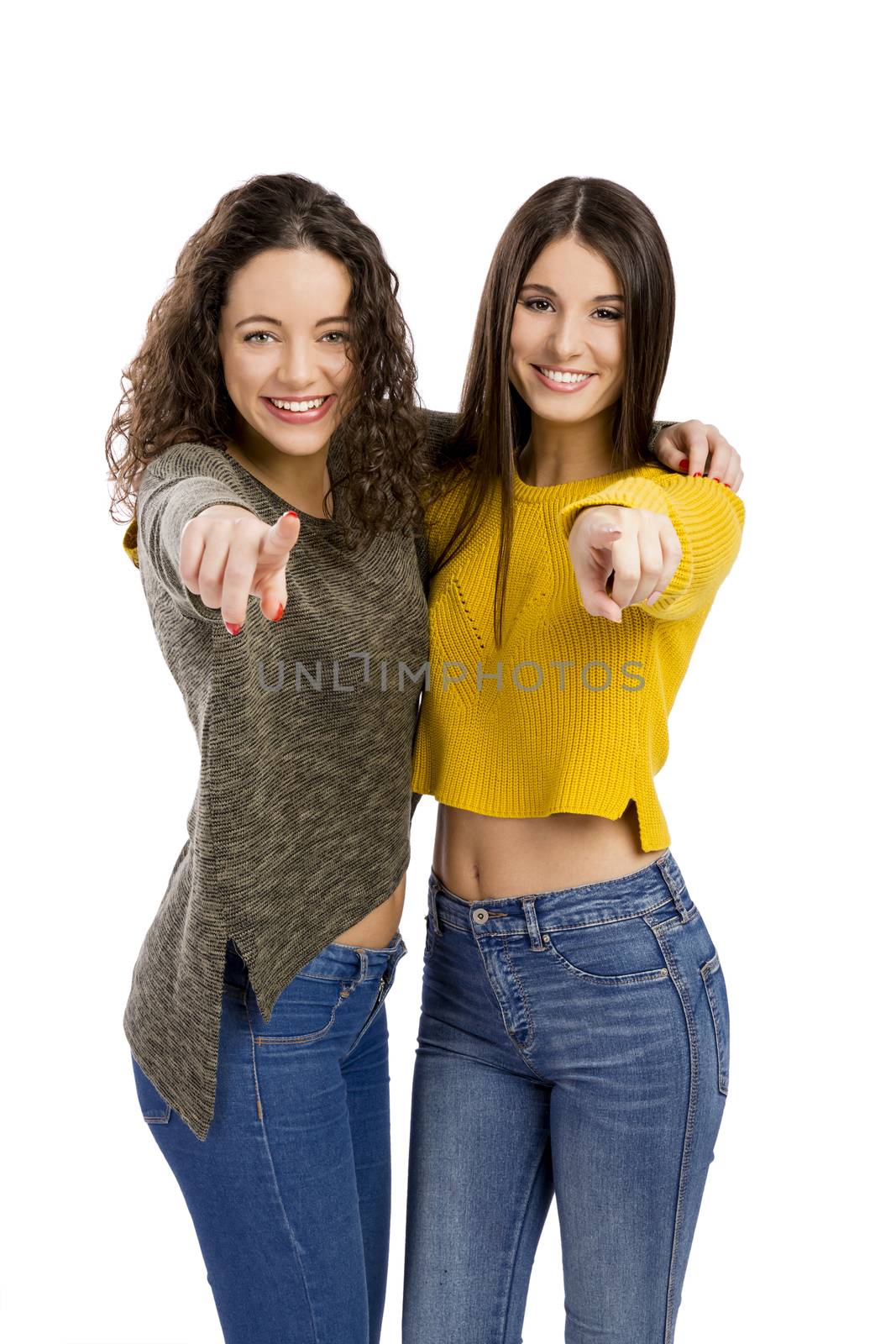 Studio portrait of two beautiful girls pointing and looking to the camera