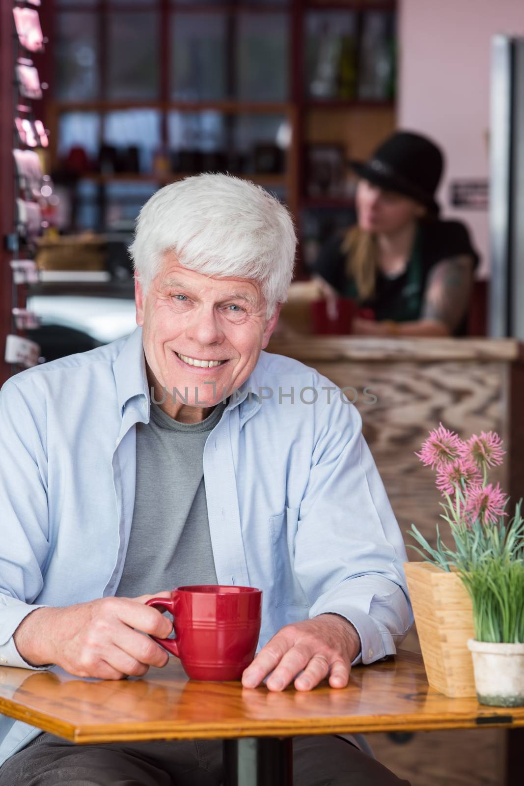 Happy senior citizen man in a coffee house with red mug