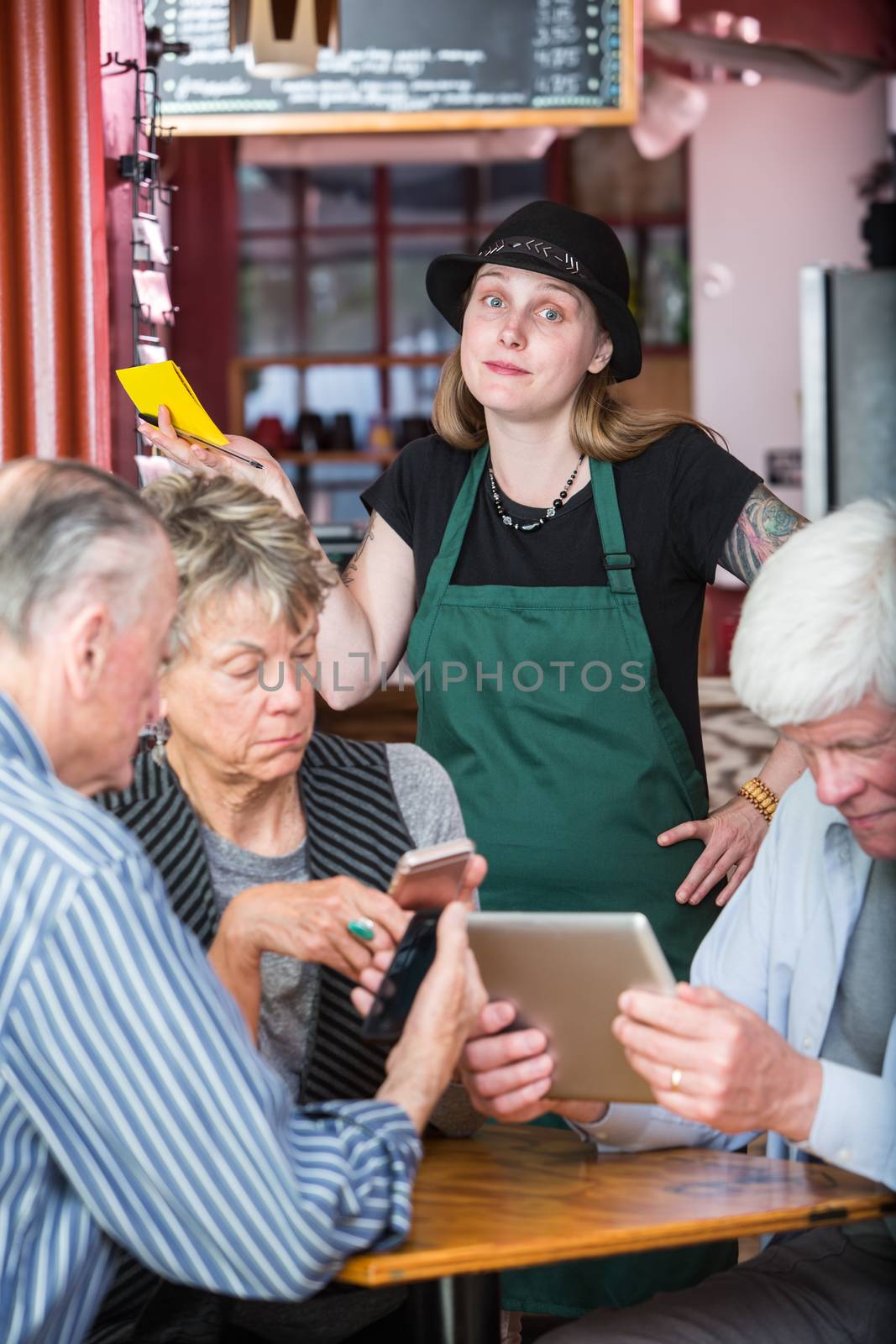 Friends in a coffee house distracted by their devices as server waits