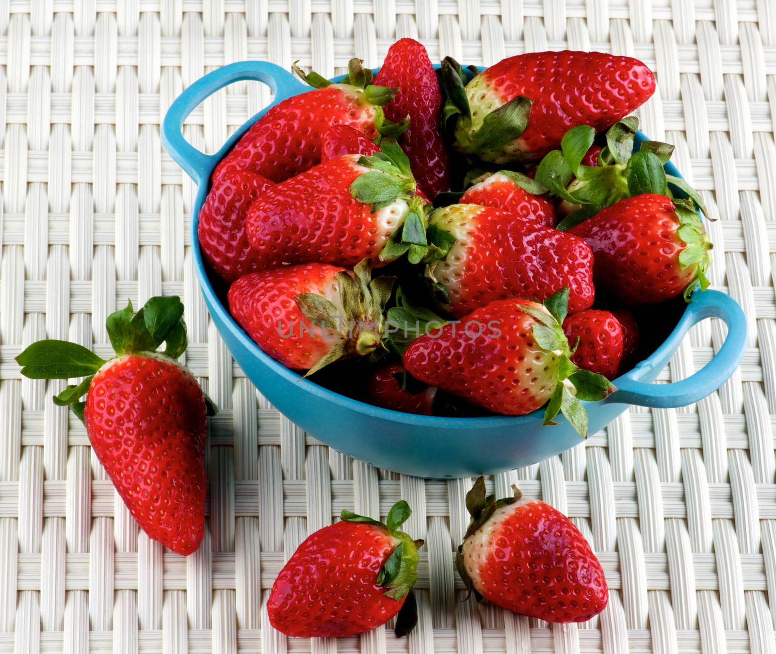 Perfect Big Ripe Strawberries in Blue Colander closeup on Wicker background