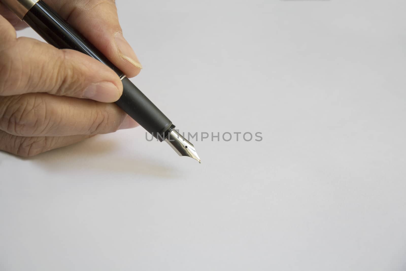 Hand holding a black pen on a white sheet of paper in the position of writing