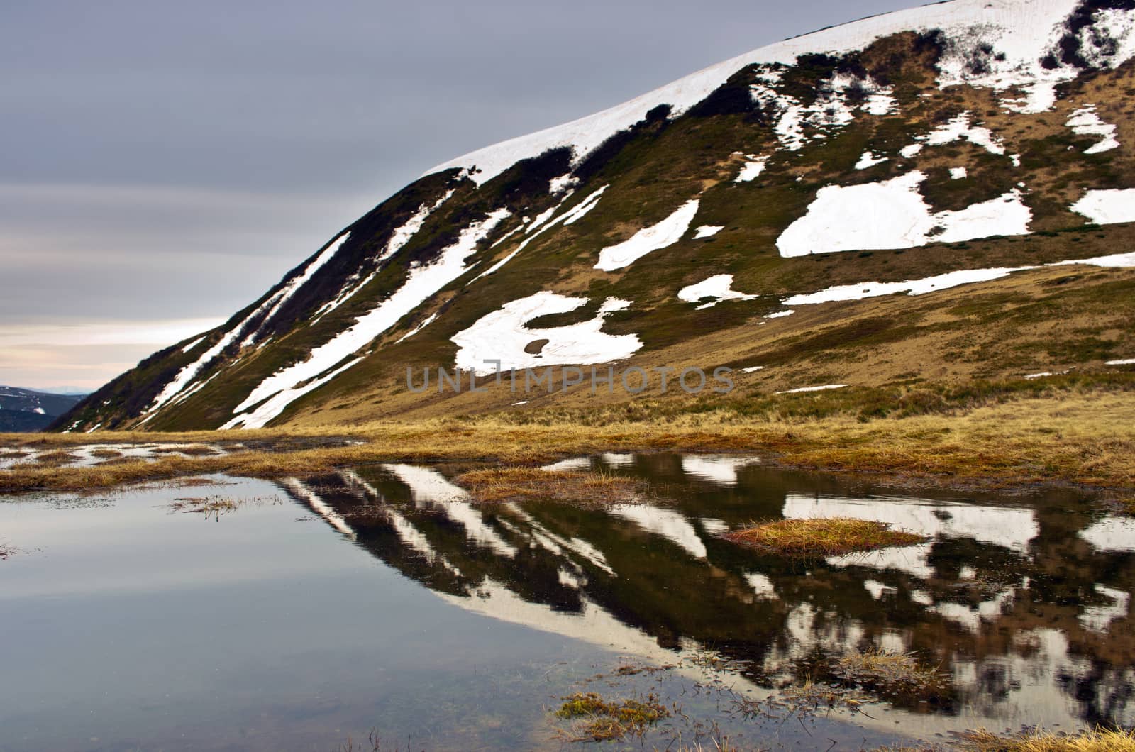 Landscape of lake with transparent water and distant mountains reflected in still morning waters