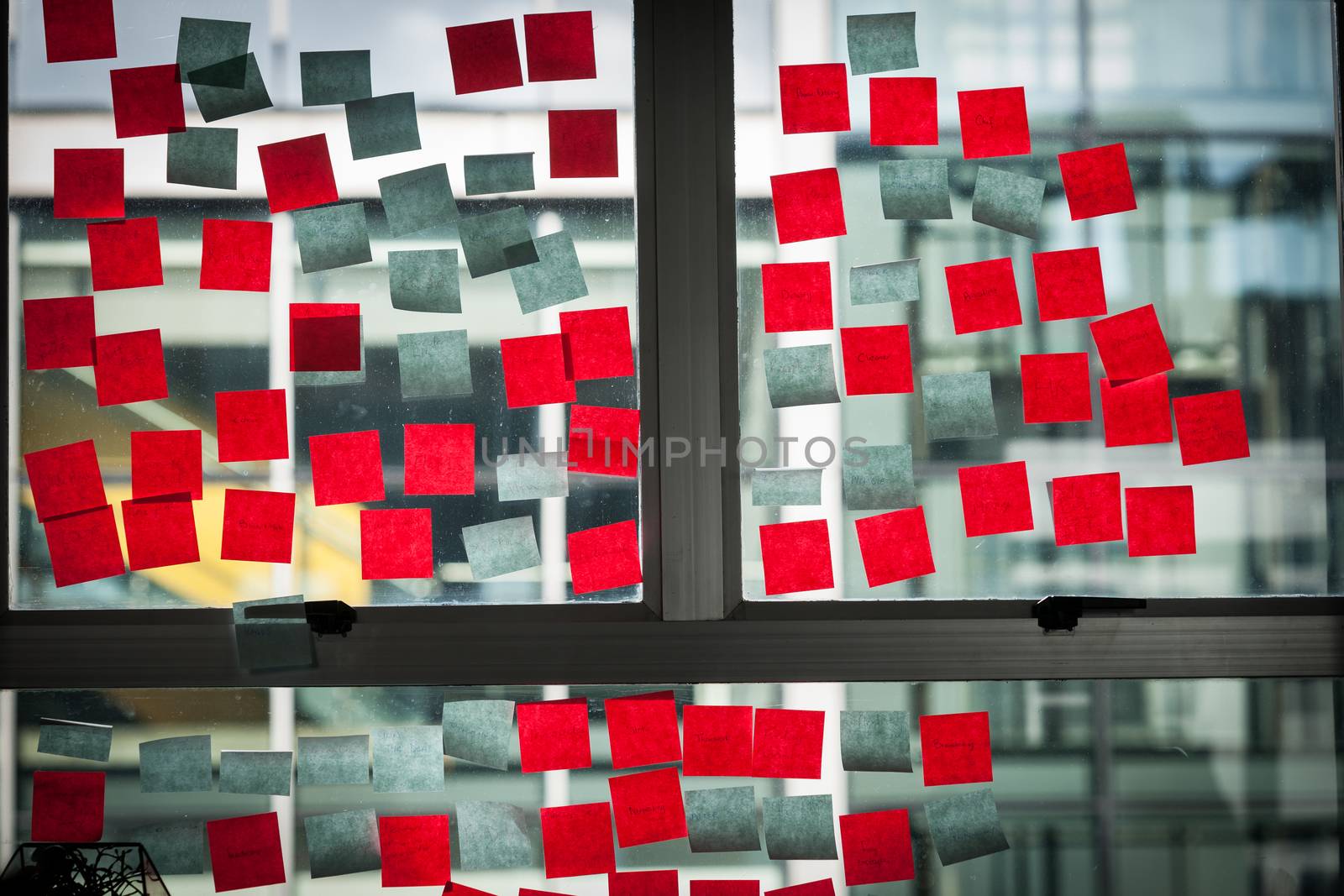 Office window used to ideas board with red and blue sticky note papers stuck to the inside looking through to next building.