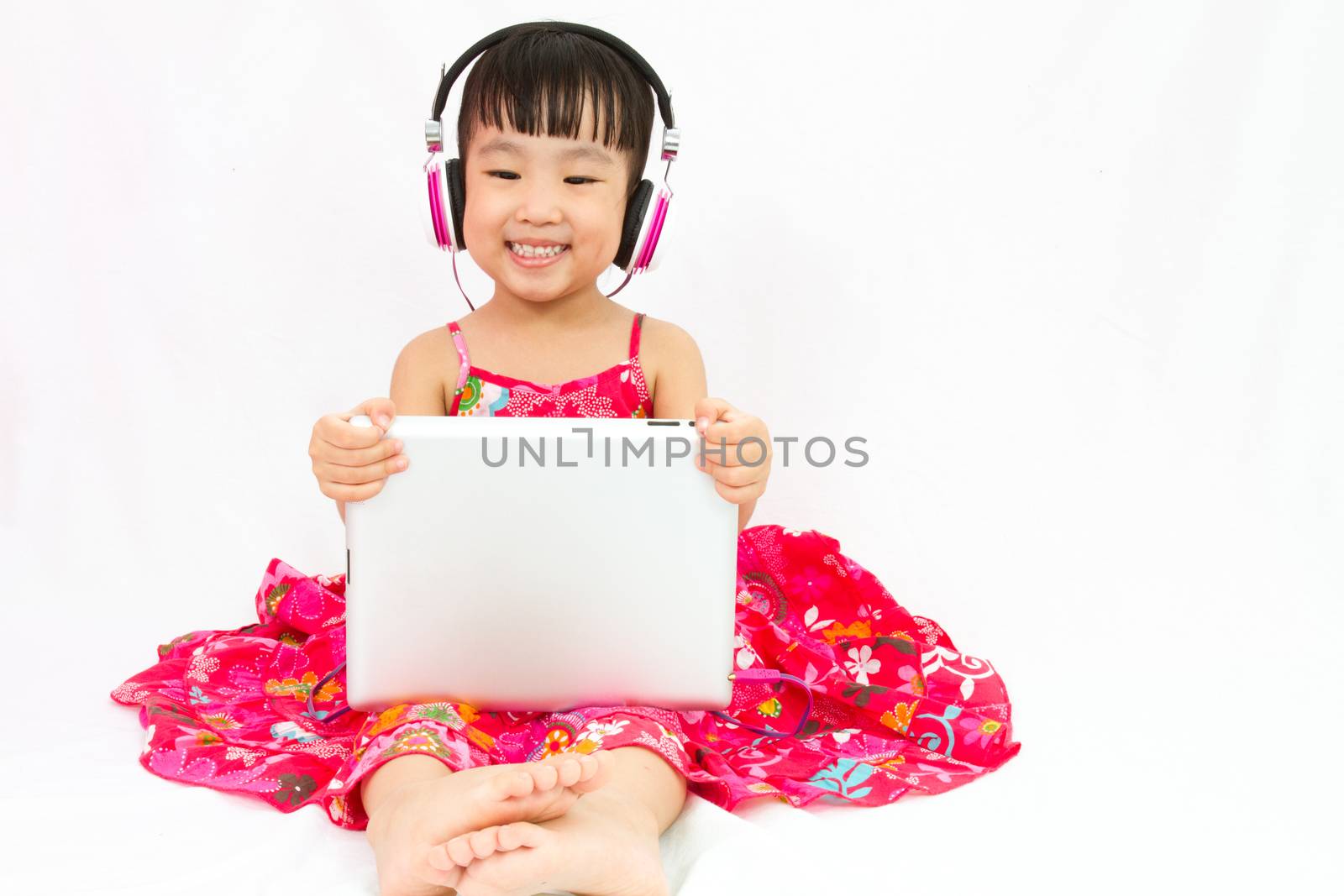 Chinese little girl on headphones holding tablet by kiankhoon