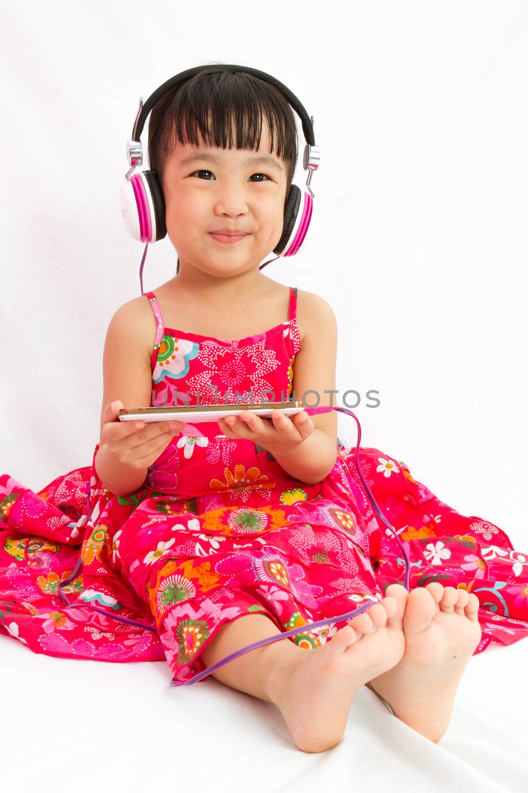 Chinese little girl on headphones holding mobile phone by kiankhoon