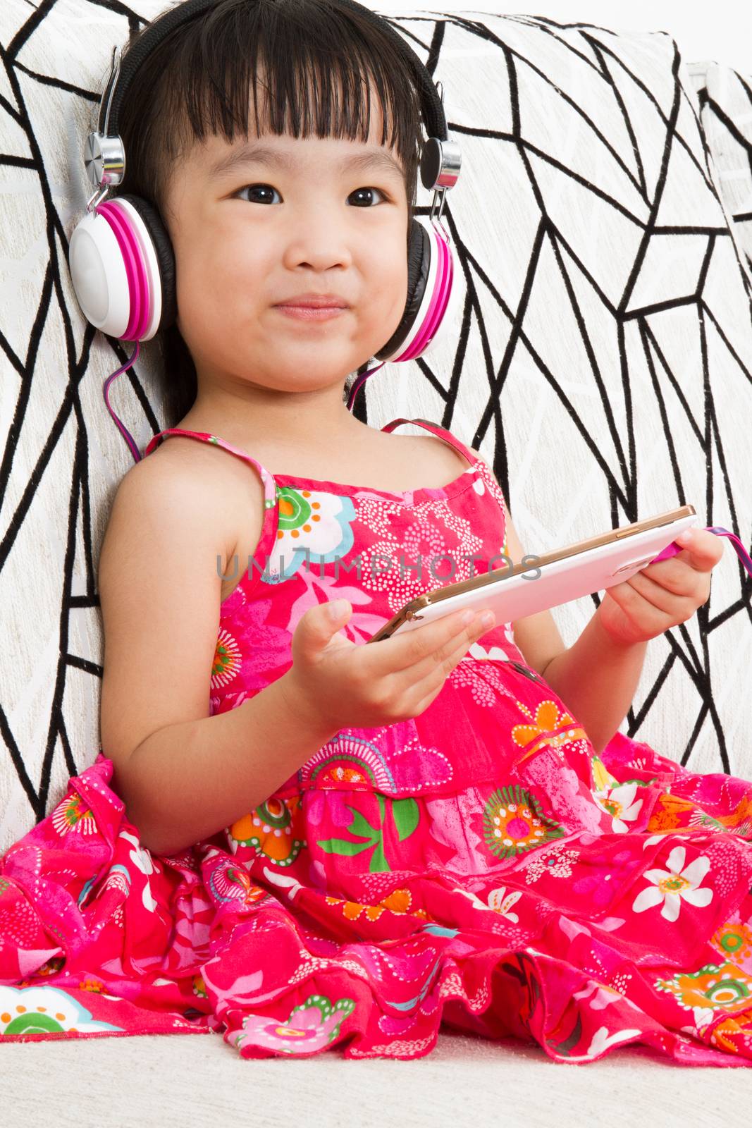 Chinese little girl on headphones holding mobile phone by kiankhoon