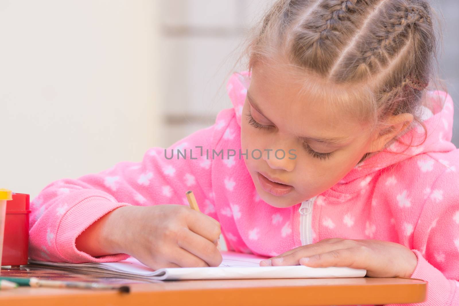 Schoolgirl is drawing in pencil on the album, in the yard